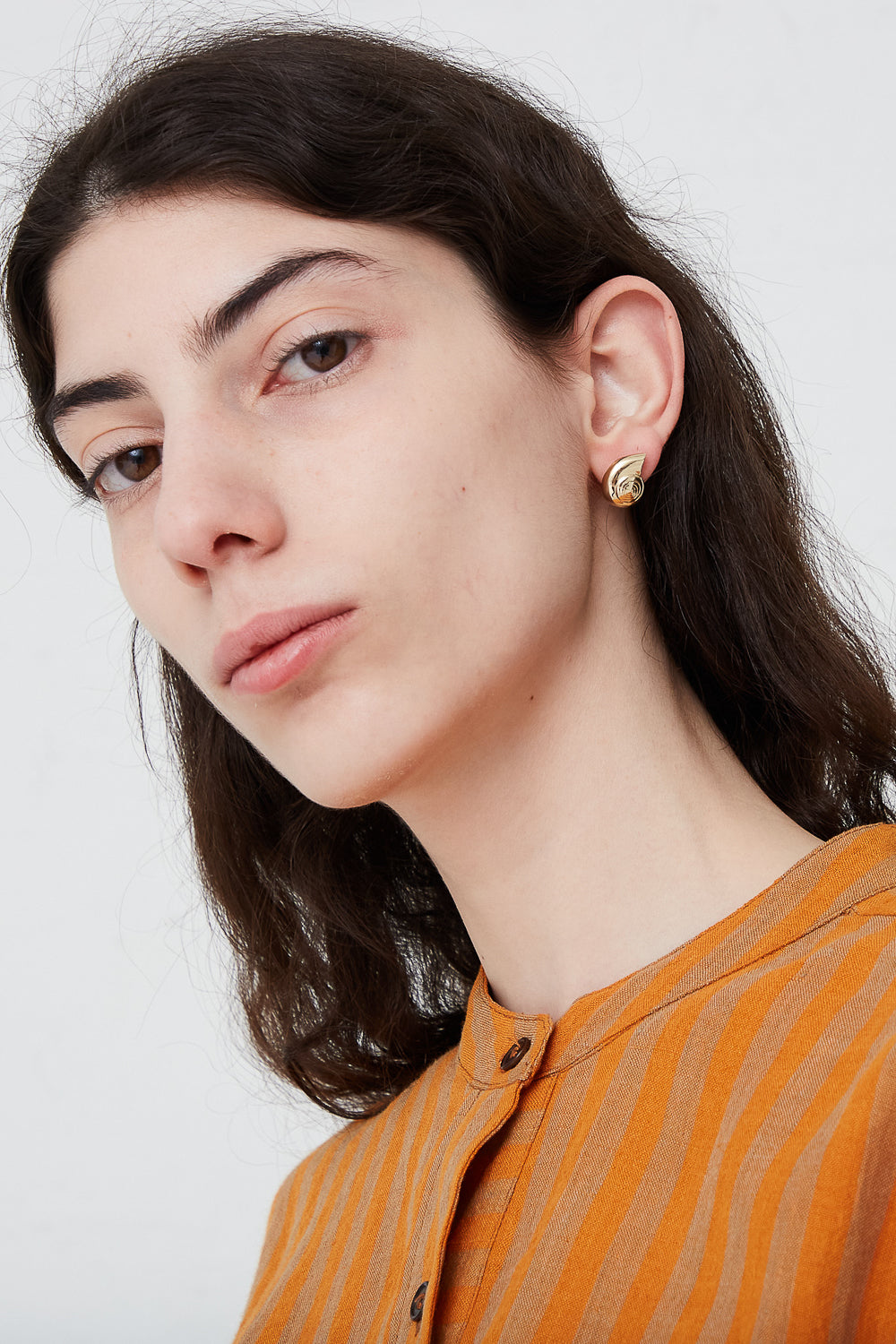 A woman wearing a pair of Large Nautilus Earrings by Kathryn Bentley, handmade in Los Angeles, complemented by an orange shirt.