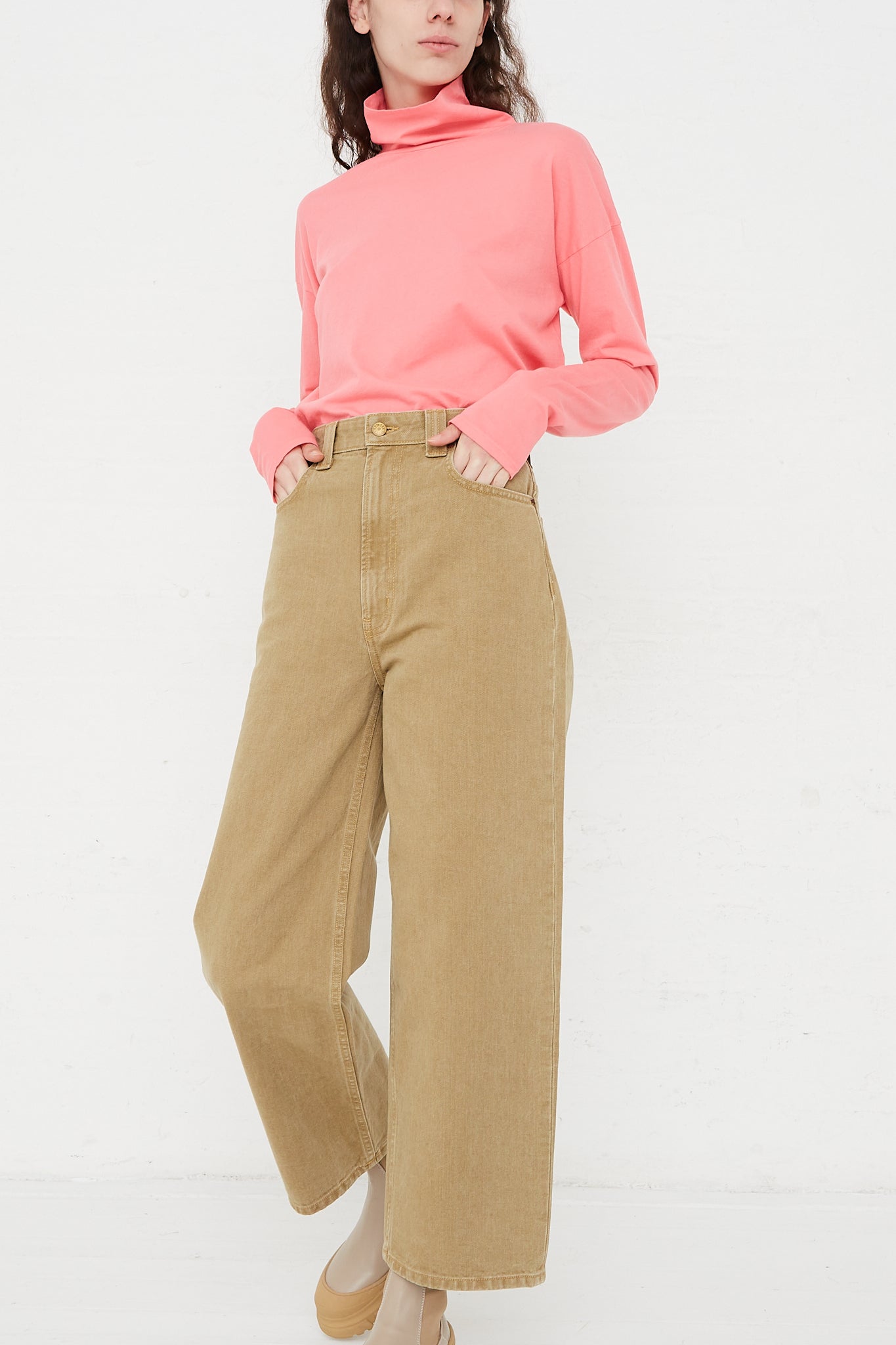 The model is wearing a pink turtle neck and tan wide leg pants by the B Sides brand.