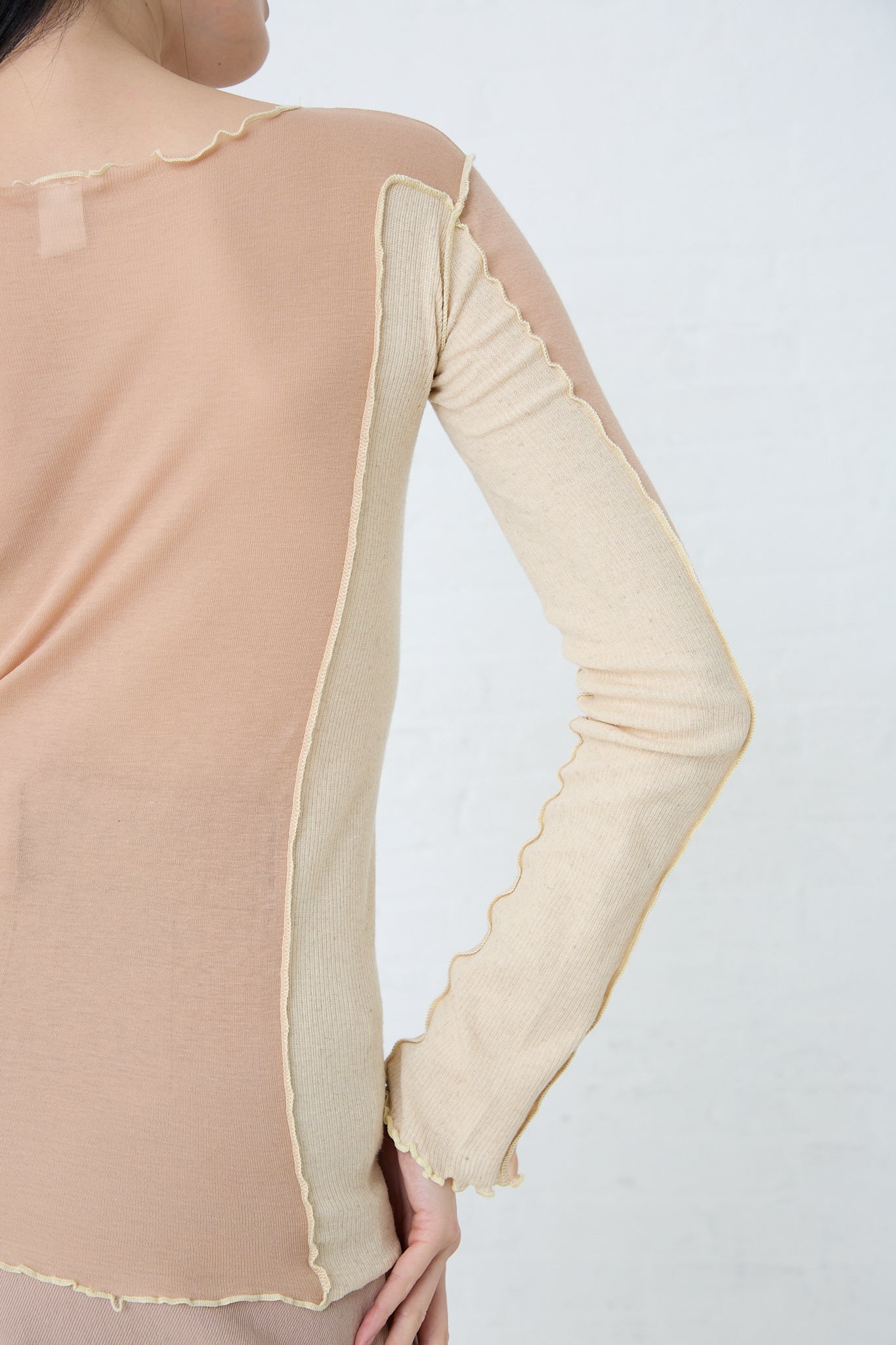 The back view of a woman wearing a Baserange Sun Longsleeve in Rosy Camel. Up close view of back and sleeve details.