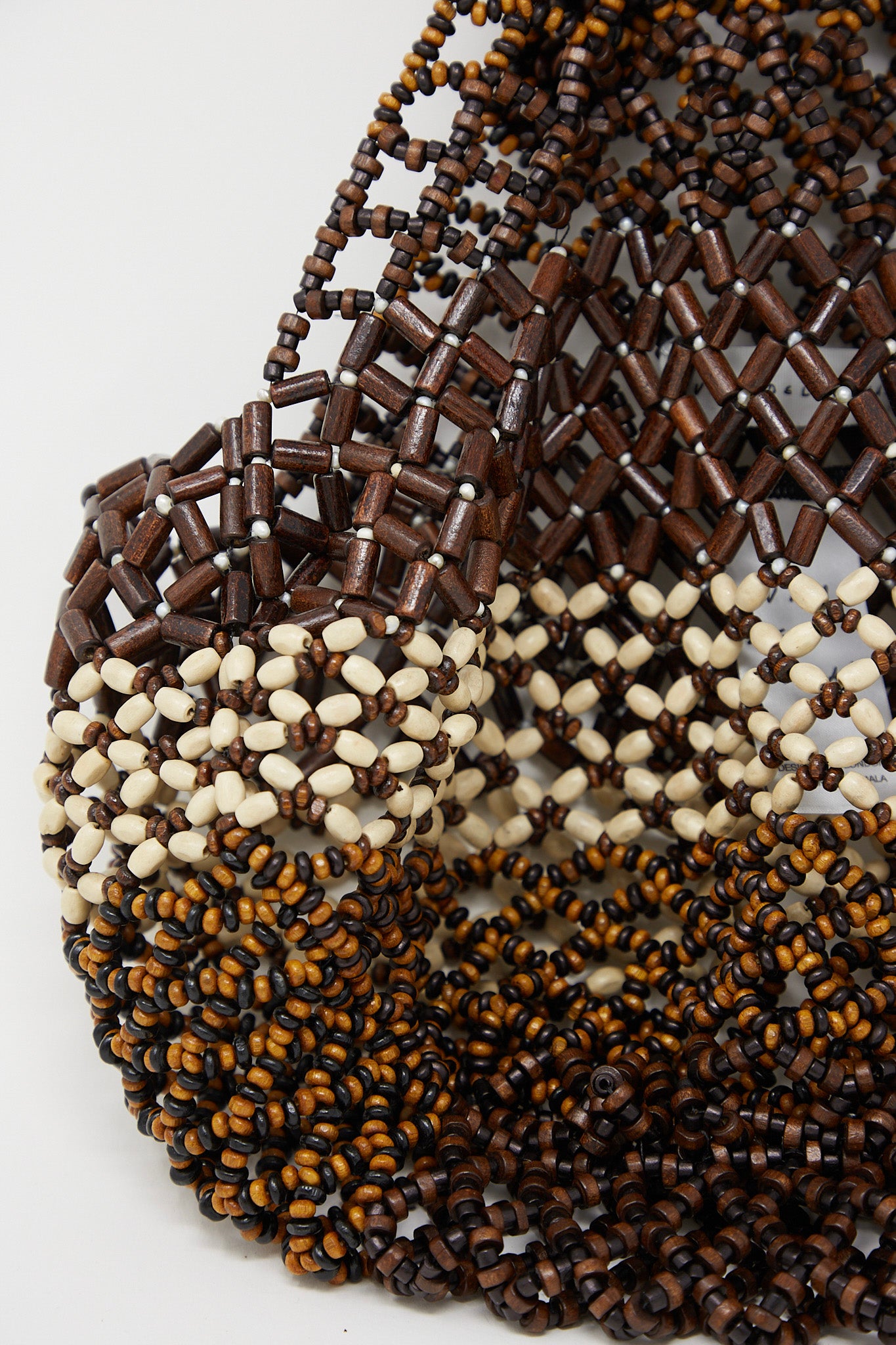 A Luna Del Pinal Medium Wooden Beaded Bag in Bone Brown, embellished with wooden beads, placed on a white surface.