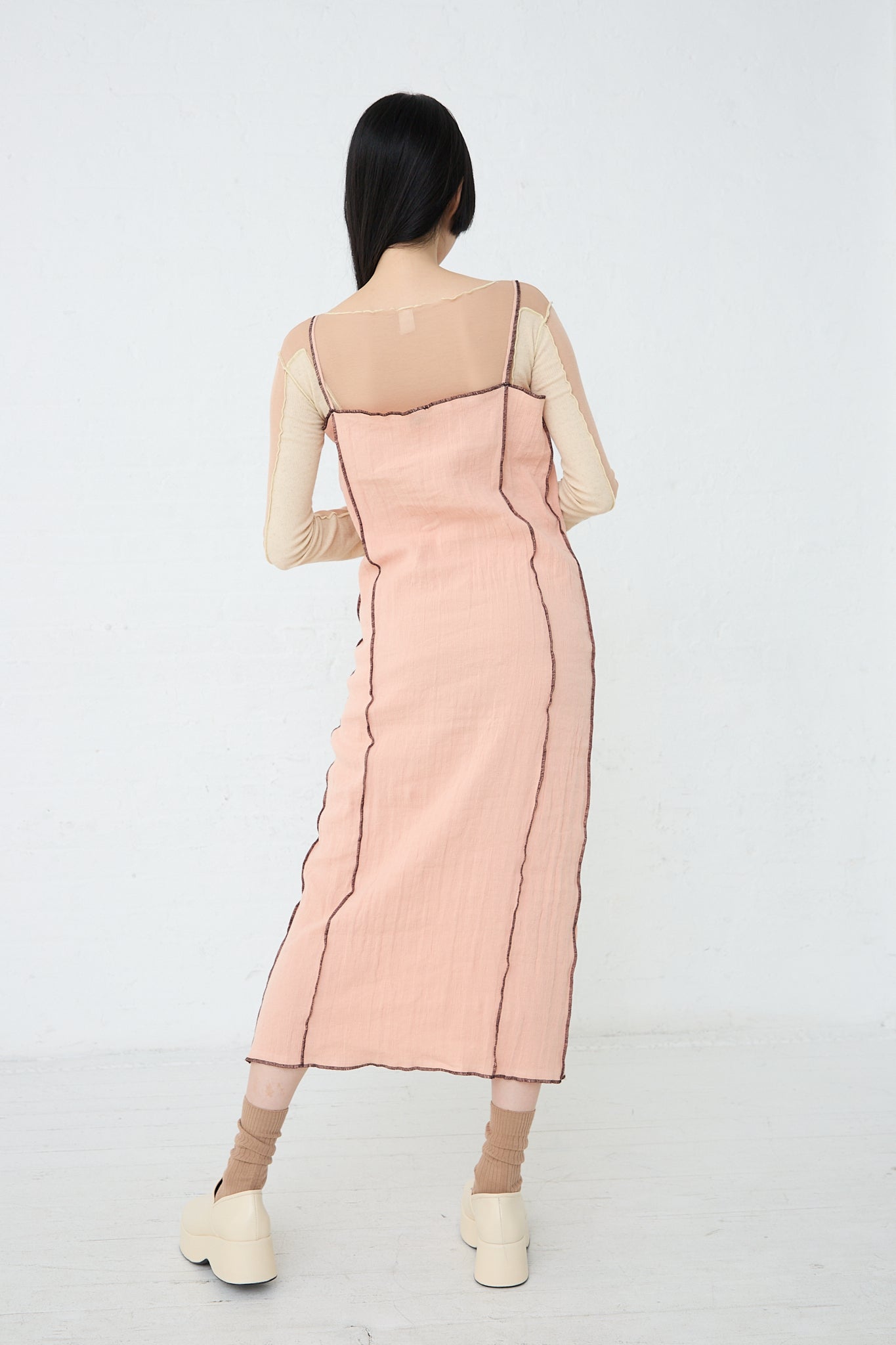 A sustainable Linen and Cotton Shok Slip Dress in Rose made by Baserange, showcasing the back of a woman in a pink dress. Back view.