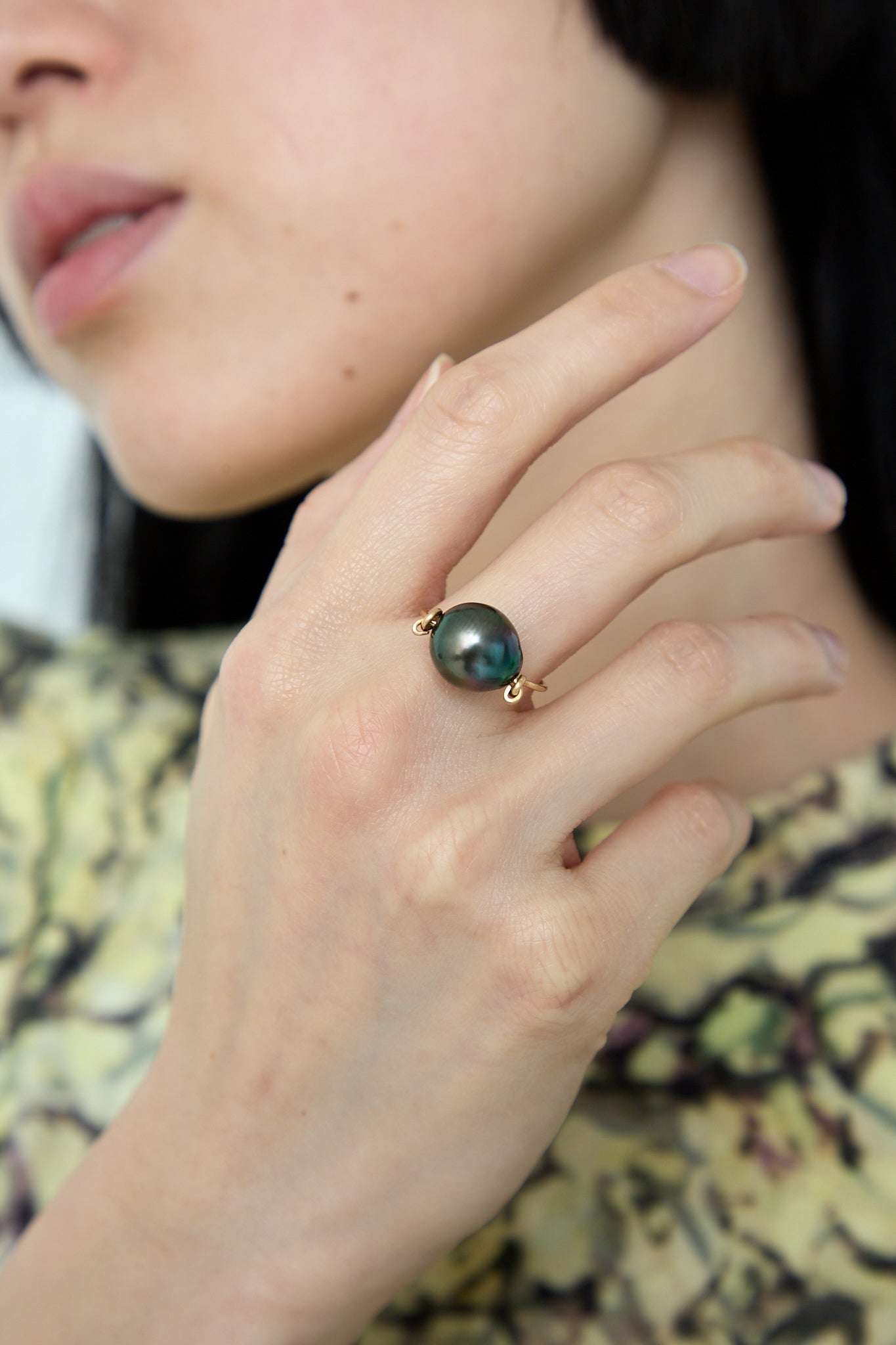A woman wearing a 14K Ring in Tahitian Pearl Charcoal adorned with a green stone (Tahitian pearl) from Mary MacGill. Up close view of hand.