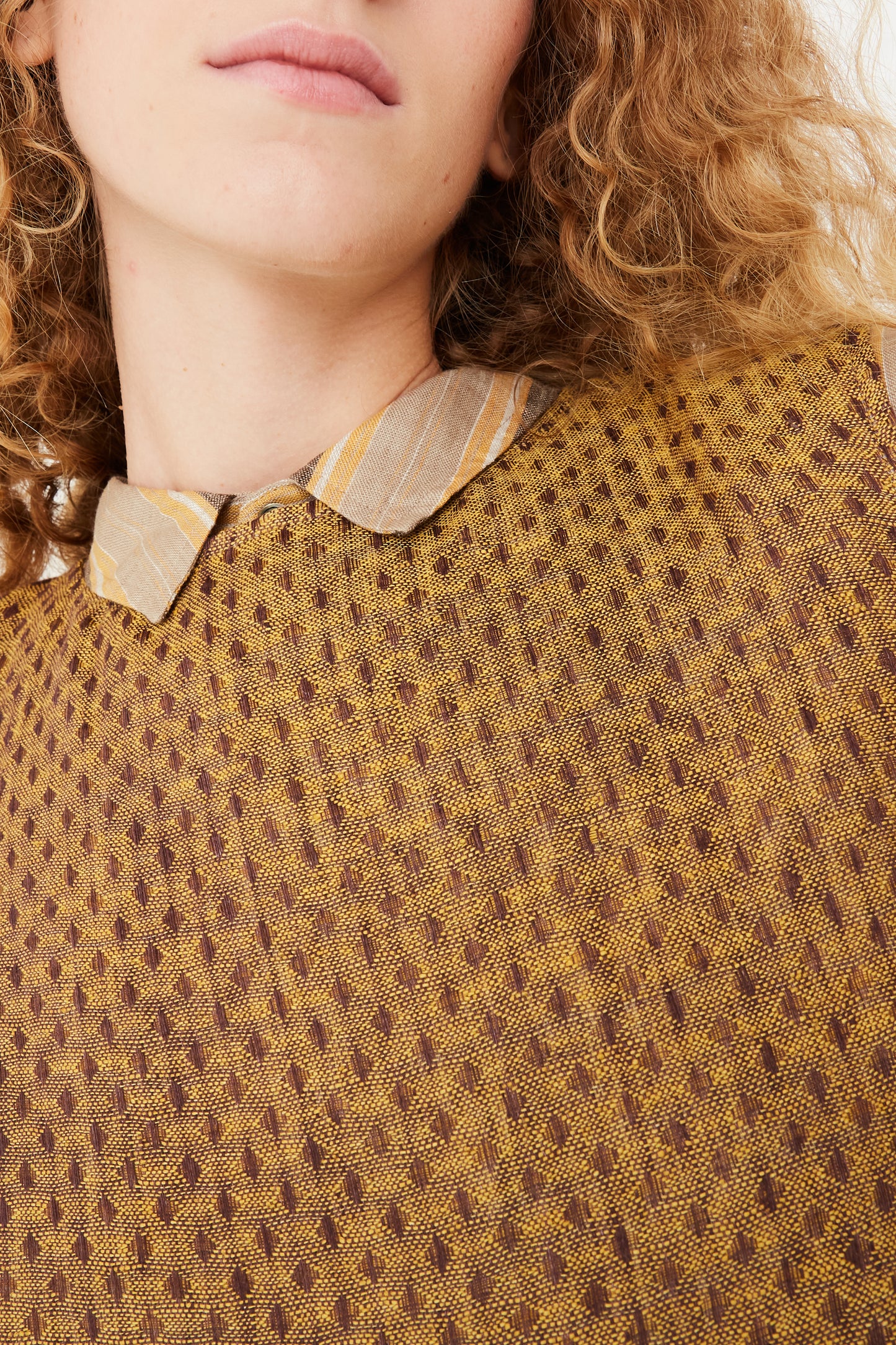 An up close view of a model wearing an Ichi Antiquités Linen Dobby Pullover in Camel and striped shirt in mustard.