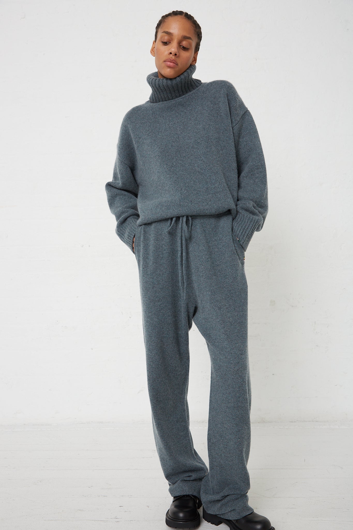 The model is wearing a grey turtleneck jumpsuit and Extreme Cashmere No. 320 Rush Trouser in Wave with a drawstring waist.
