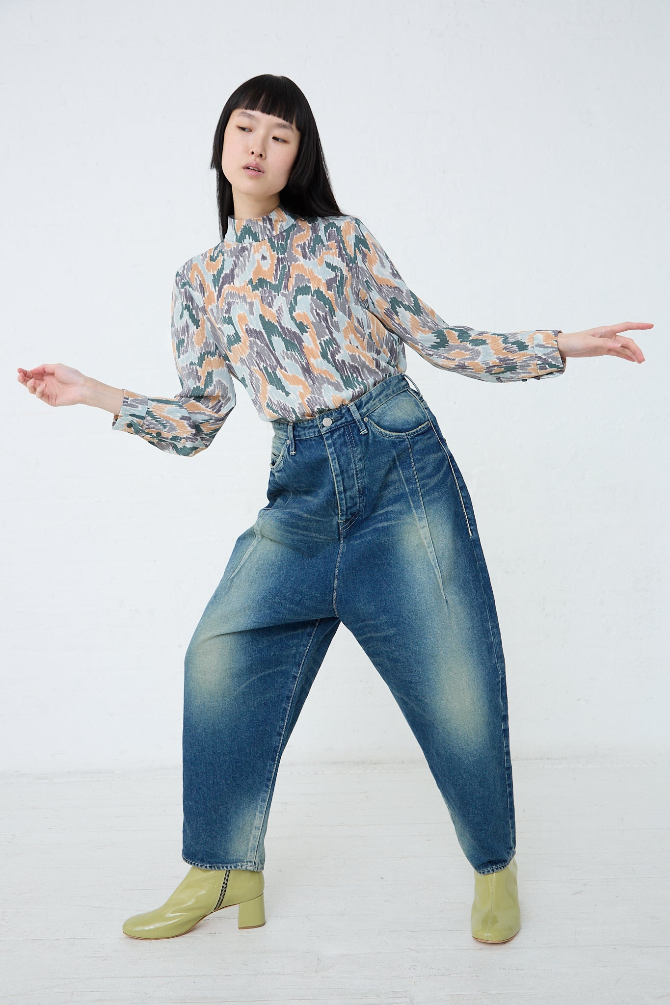 A woman wearing a Mina Perhonen Always New Tapered Pant in Blue denim and blouse. Front view. Model's arms are raised.
