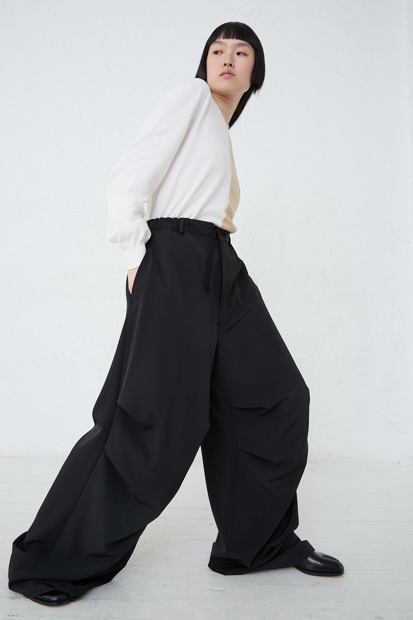 A woman in a white shirt and MM6 black drawstring waist pants. Full length and side view.