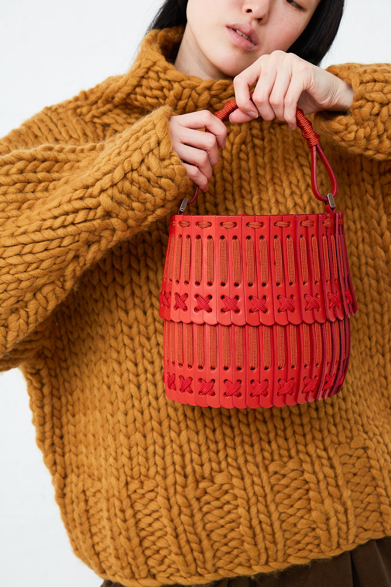 A woman is holding a Hatori Bucket Bag 80 in Amaranto, Cherry and Tangerine.