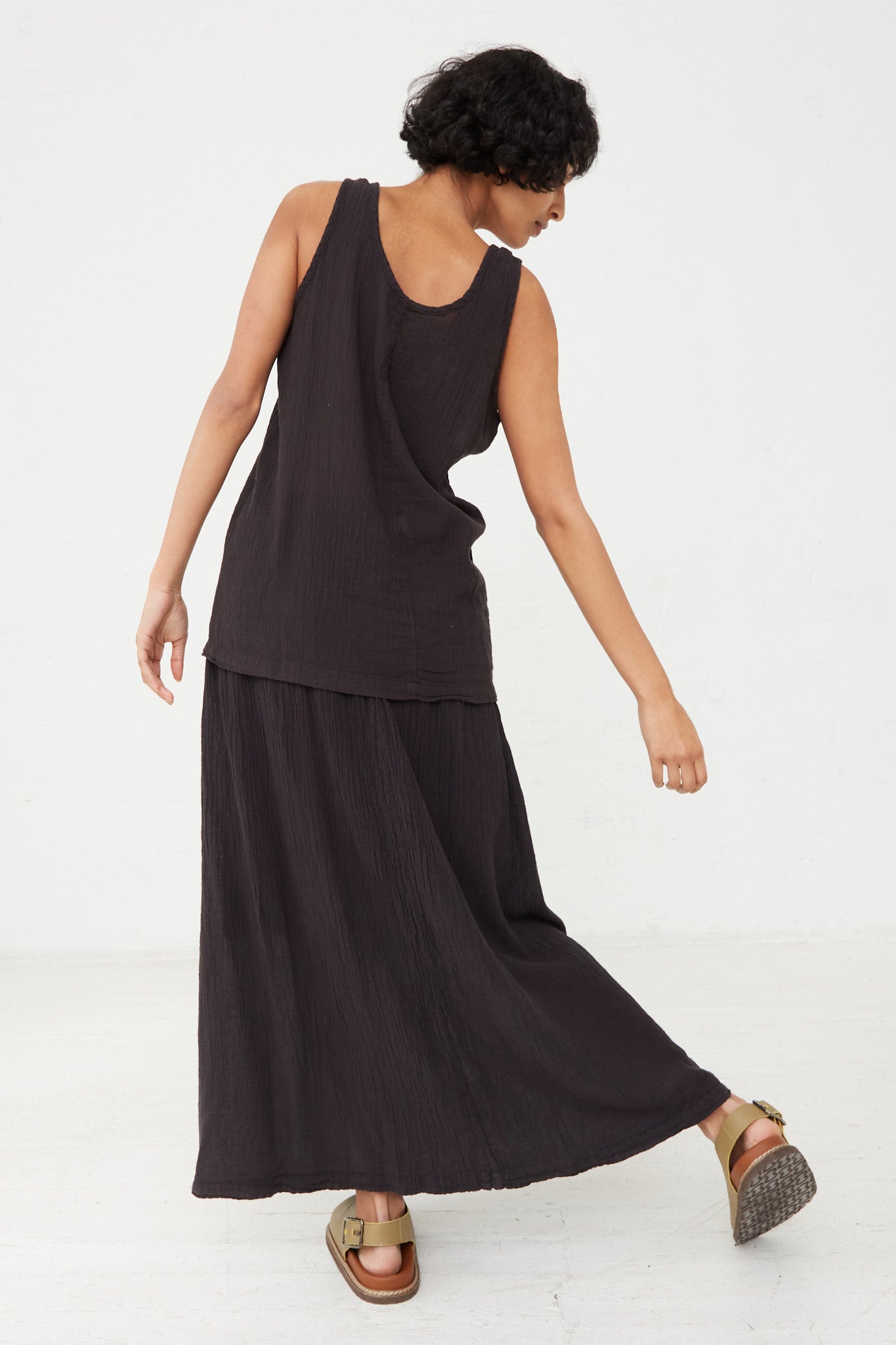 The back view of a woman wearing a Black Crane relaxed fit scoop neck tank top in Black. Full length.