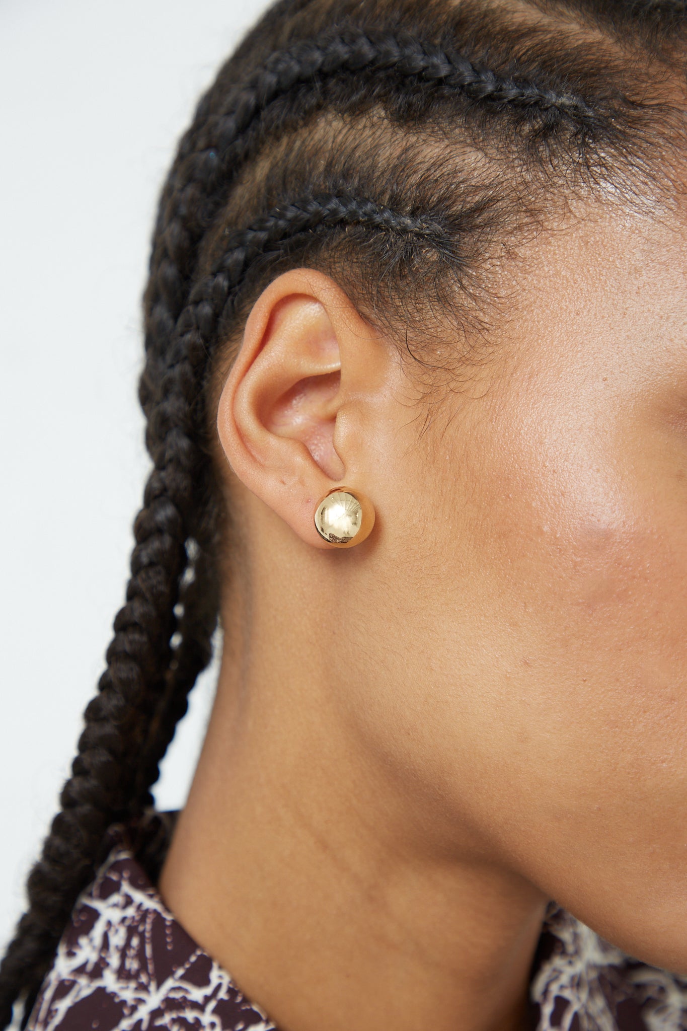 A woman with braided hair wearing the Kathleen Whitaker Sphere Stud Large 12mm Single Earring in 14K Yellow Gold.