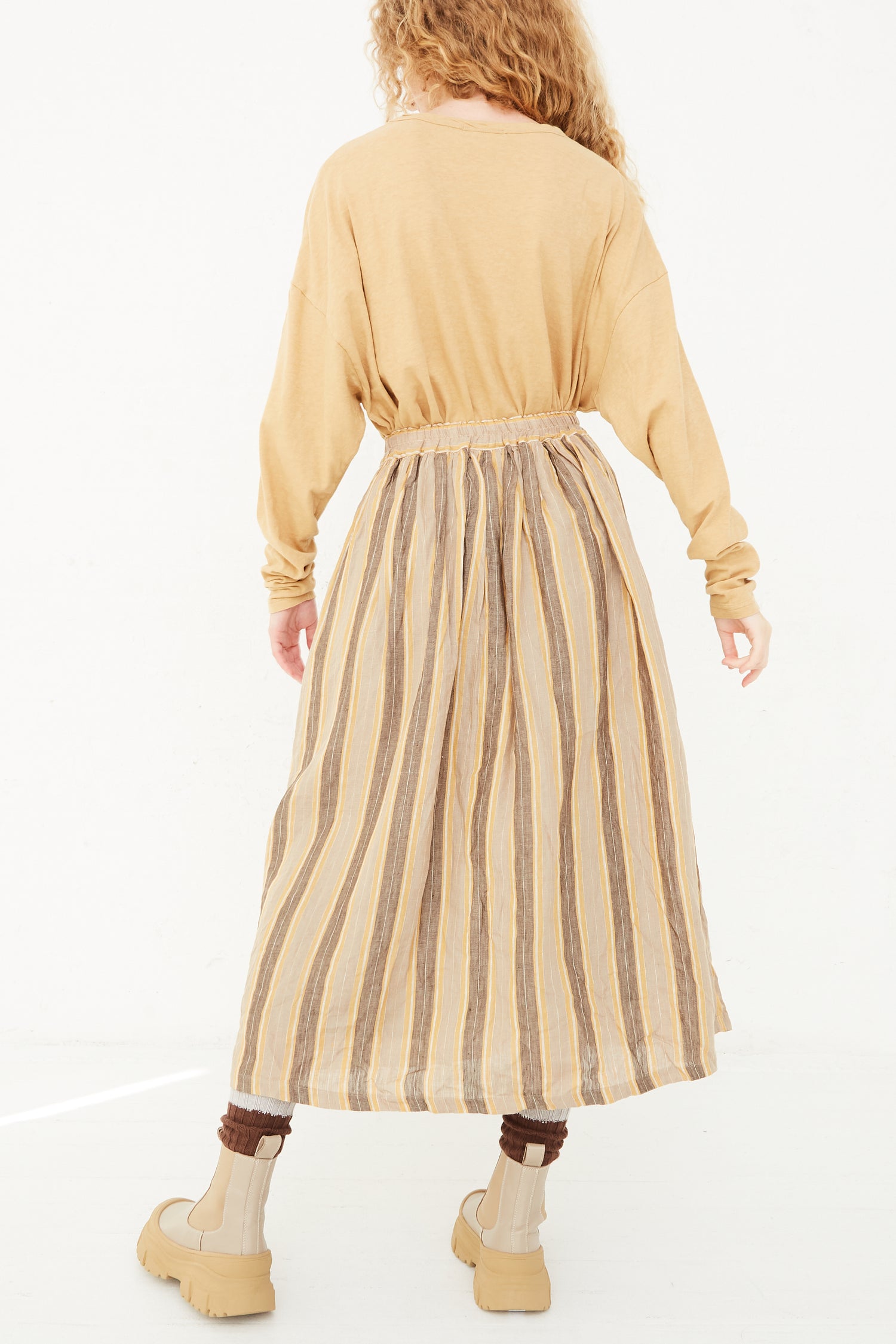 The back view of a model wearing a long, Ichi Antiquités Linen Stripe Skirt in Mustard with an elasticated waist.