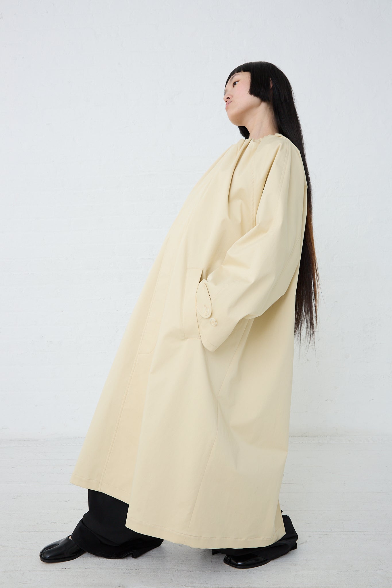 A woman is posing in a MM6 Pale Yellow Trench Coat. Side view.