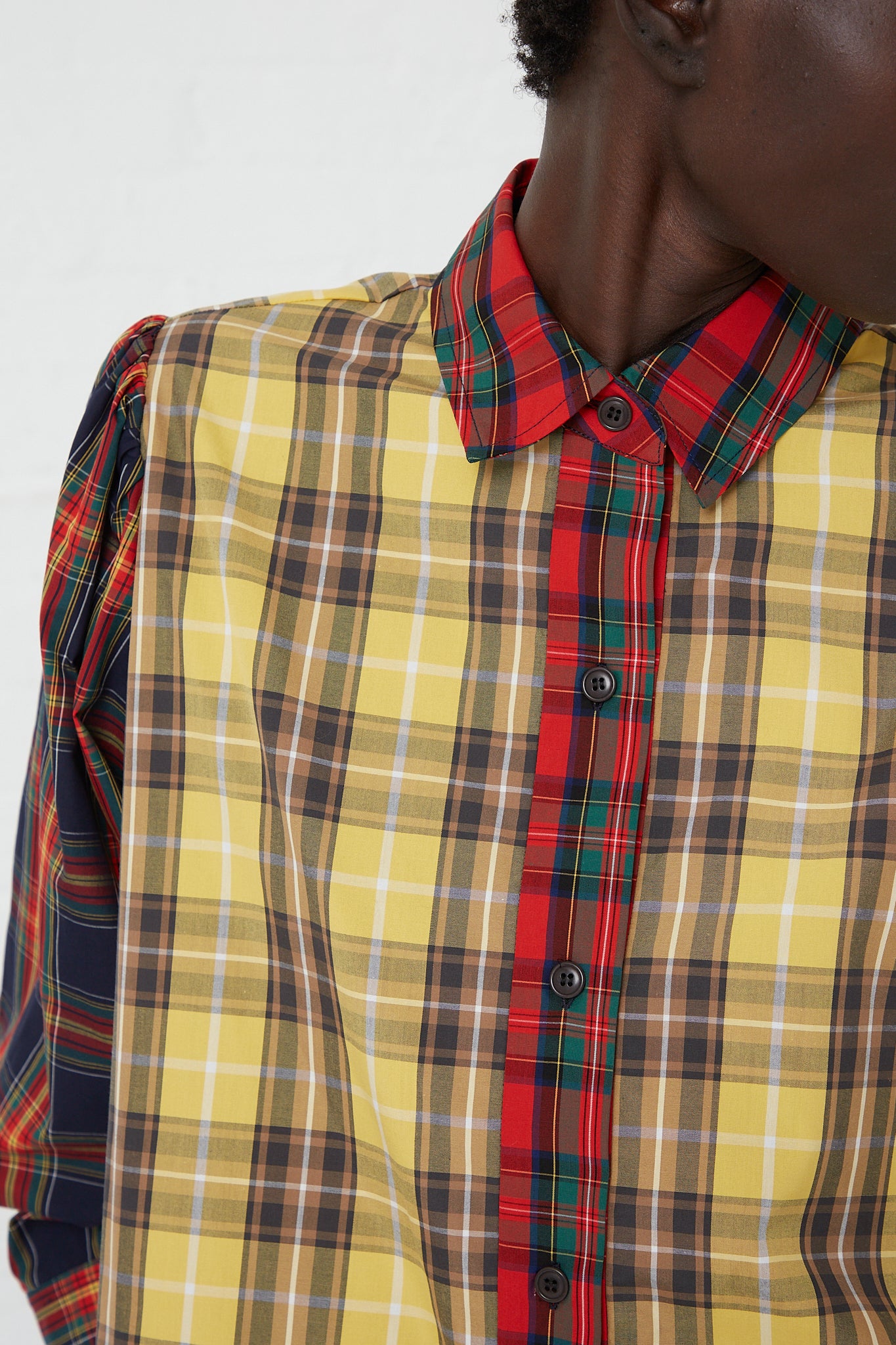 A woman wearing a long sleeve KasMaria Cotton Poplin Ruffle Shirt in Mix Plaid, made of patchwork Japanese cotton, featuring a ruffled hem, in yellow and red plaid.