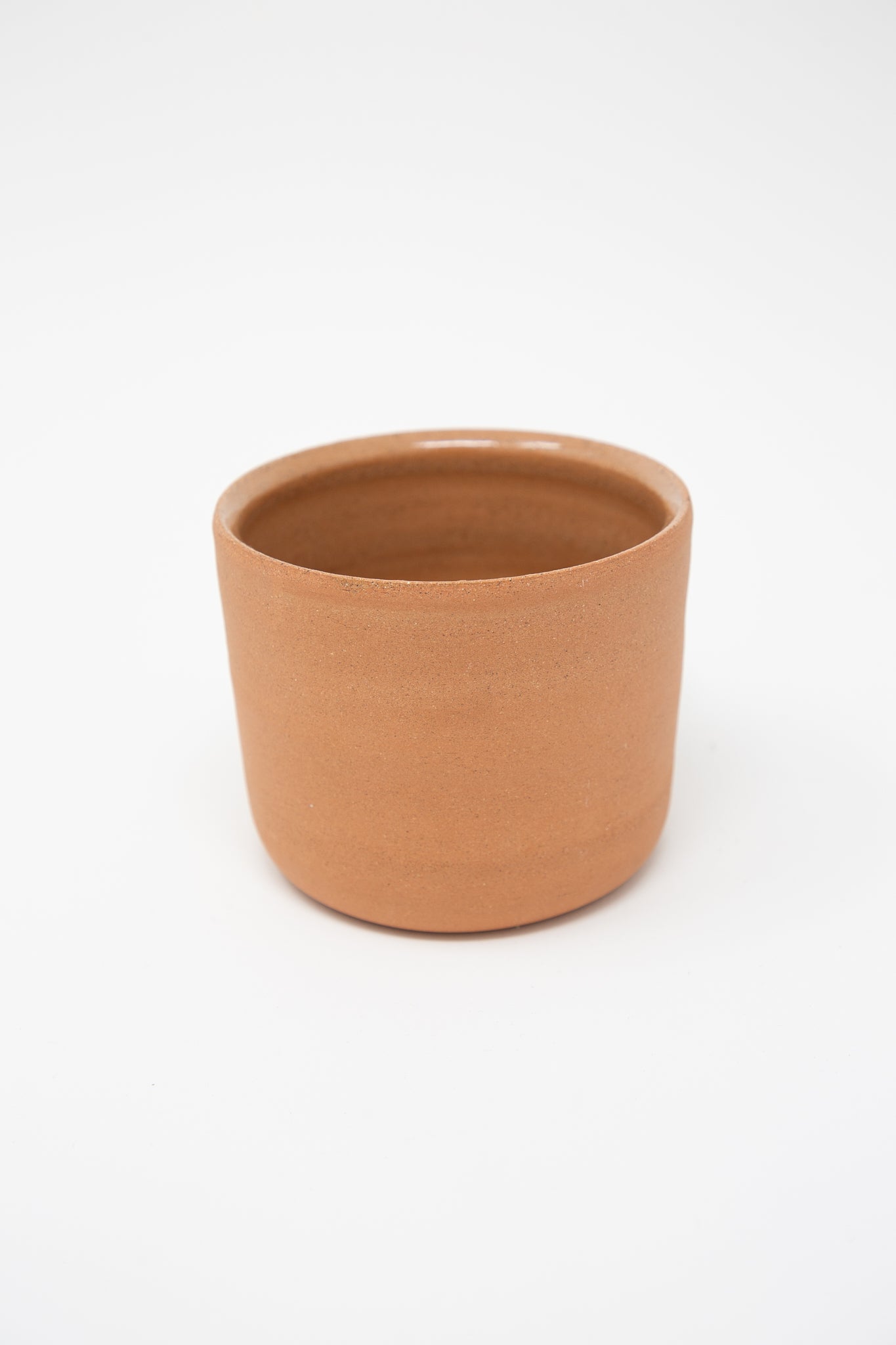 A small handmade Lost Quarry terracotta mug on a white background. Back view.