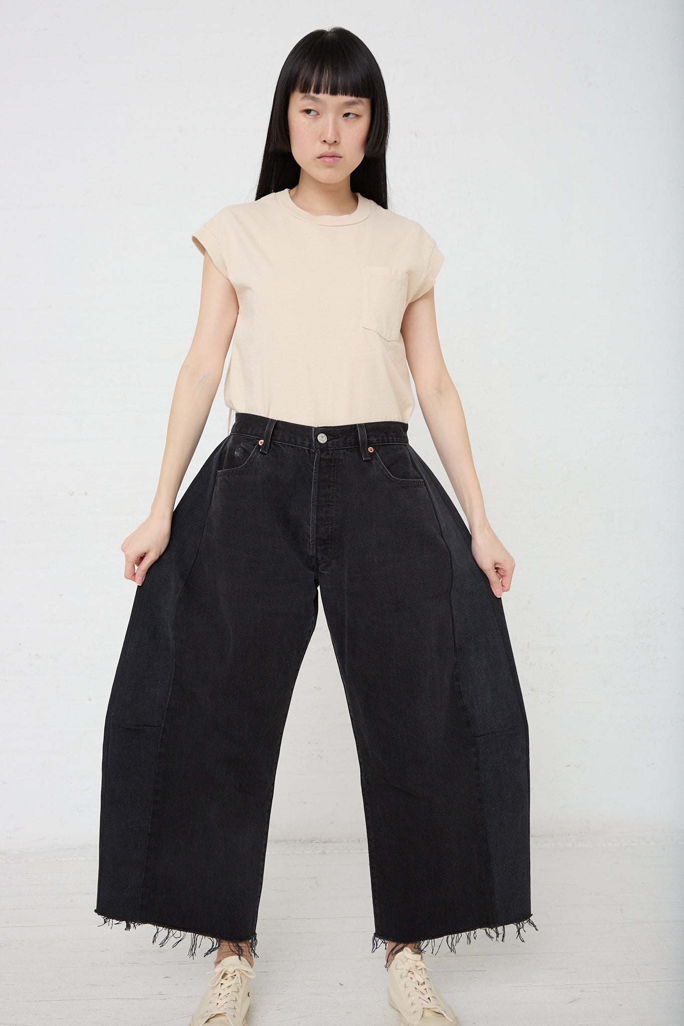 A woman showcasing a pair of B Sides vintage black denim wide leg pants in Lasso with a slouchy fit and a cutoff frayed hem.