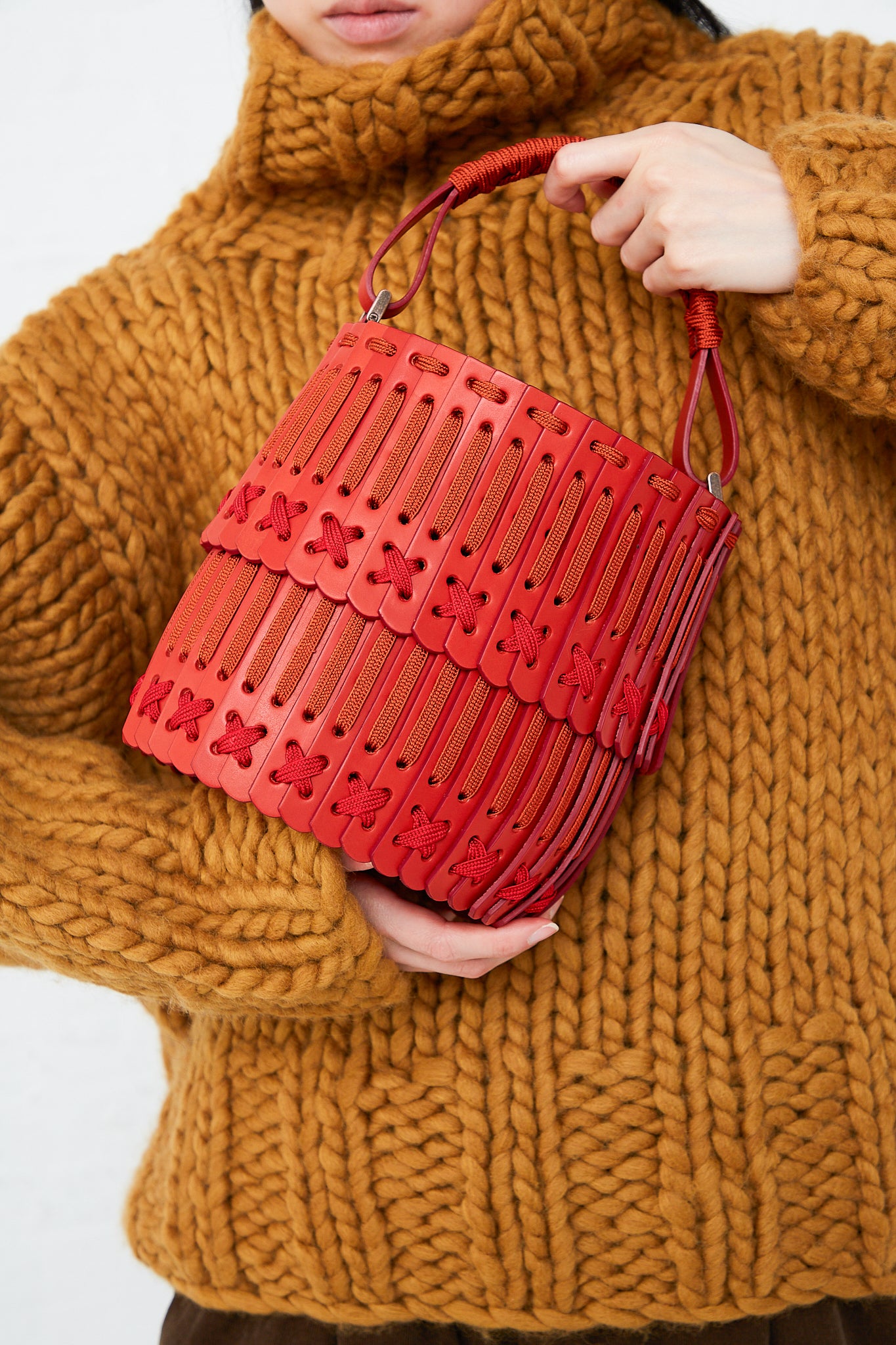 A woman is holding a Hatori Bucket Bag 80 in Amaranto, Cherry and Tangerine.