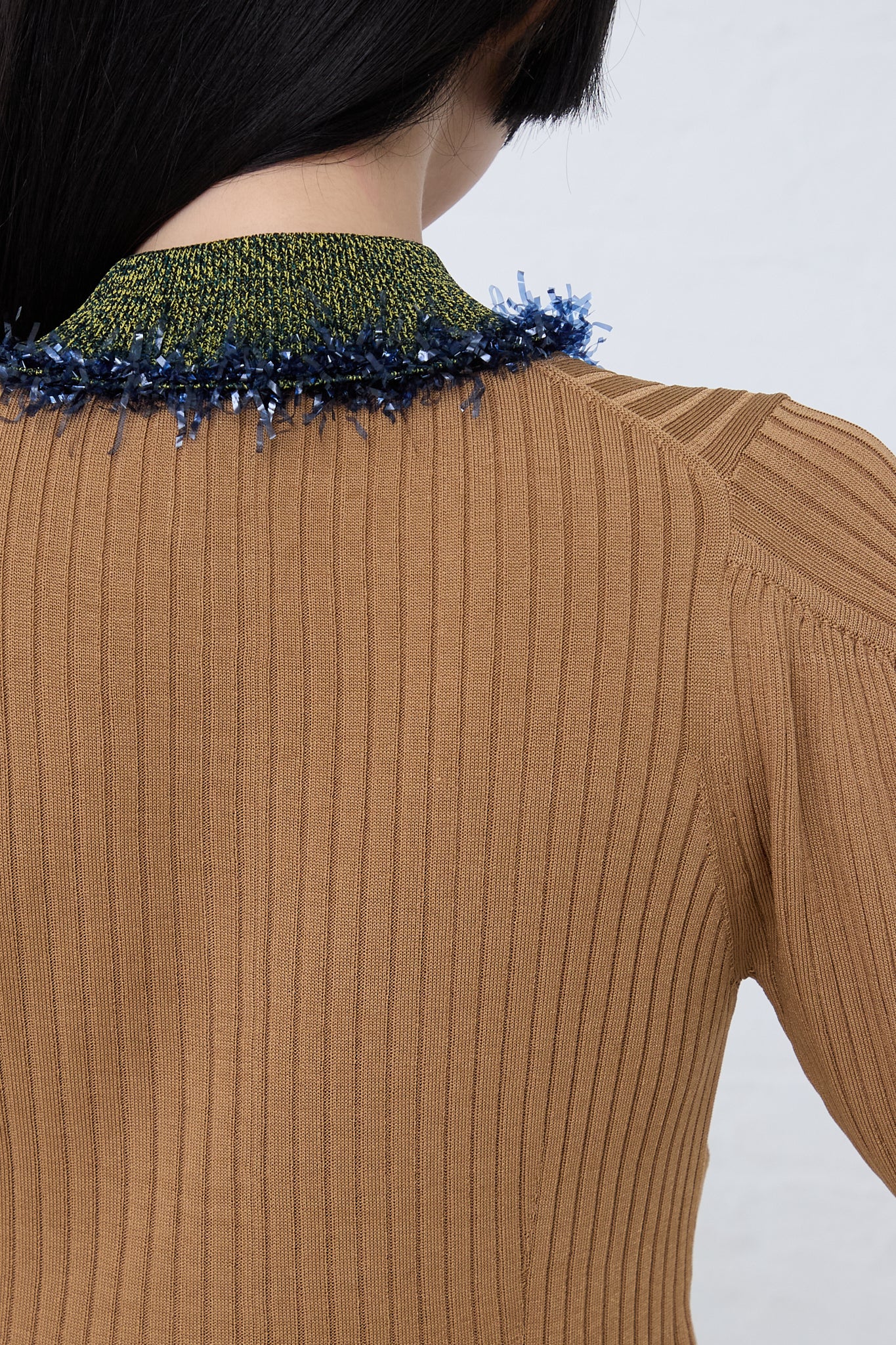 The back view of a woman wearing a TOGA PULLA Wide Rib Knit Cardigan in Beige with blue trim.