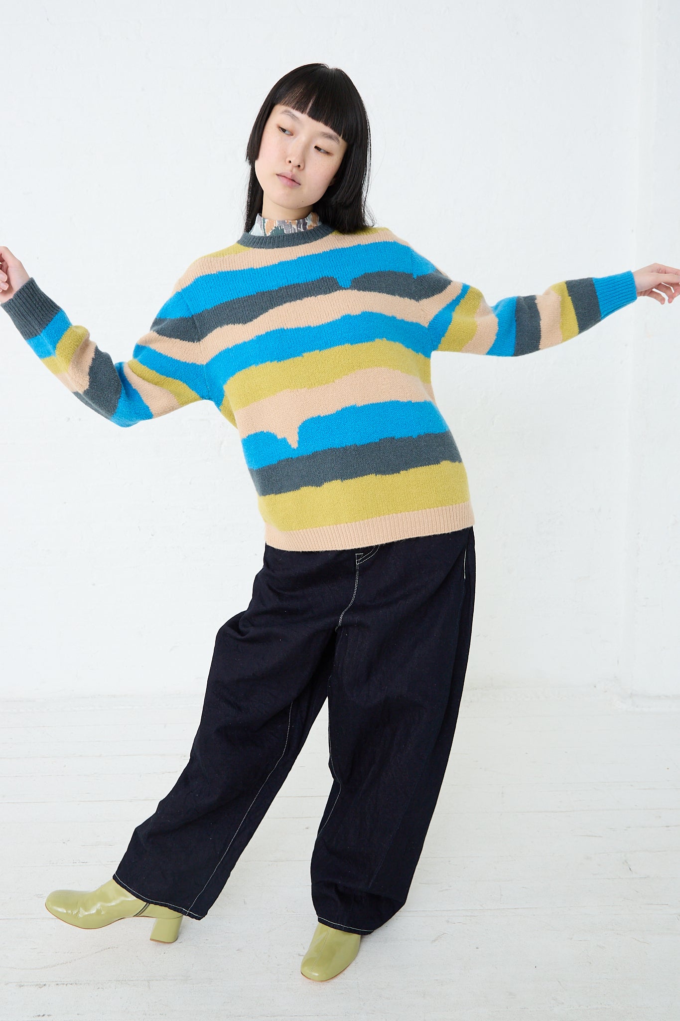 A woman wearing a Mina Perhonen Light Wind Sweater in Blue Mix, which is a blue and yellow alpaca/wool blend sweater with stripe design. Front view and full length.