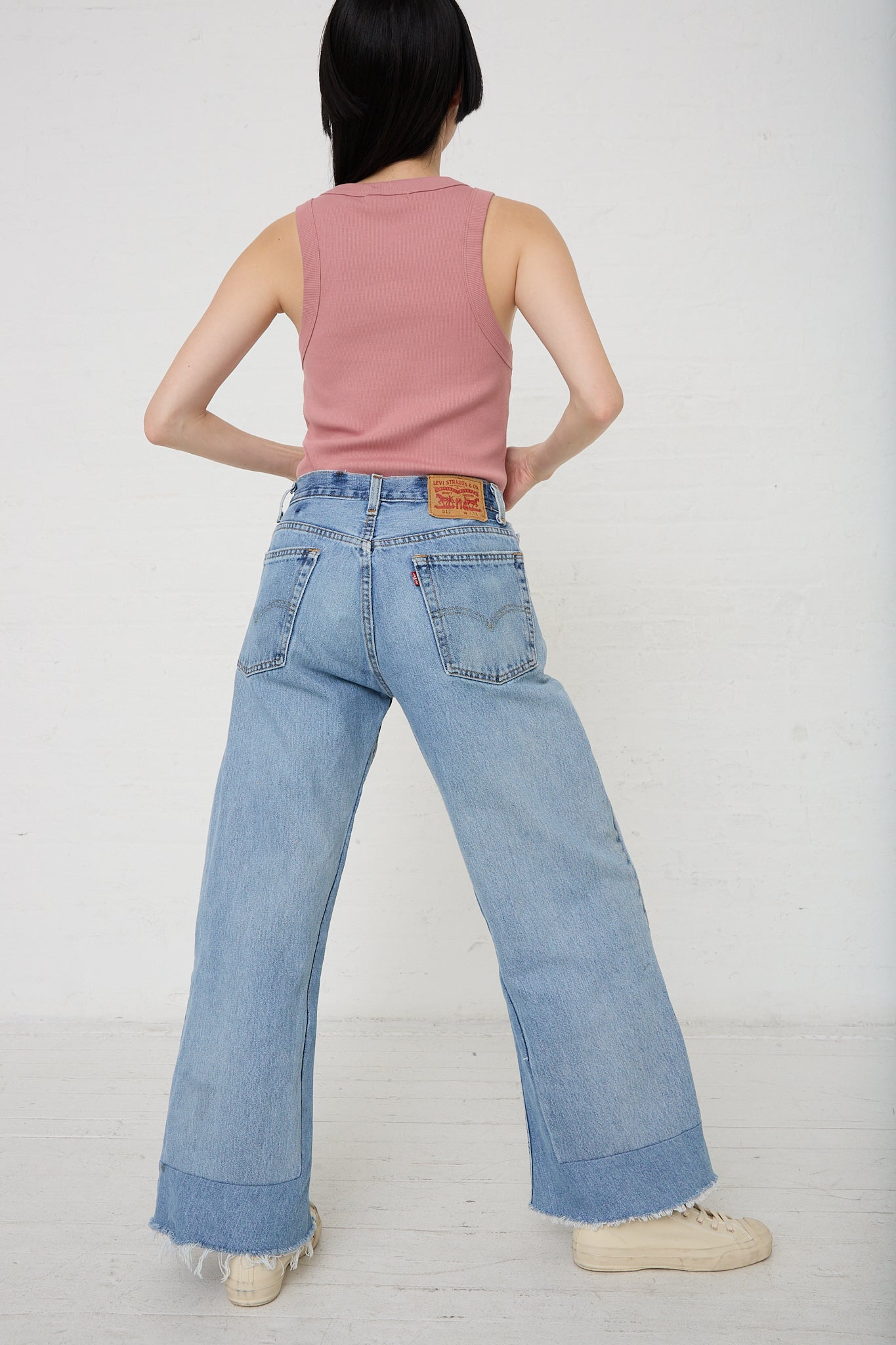 A woman wearing a pink tank top paired with B Sides' Reworked Culotte in Vintage Indigo denim flared jeans. Back view and full length.