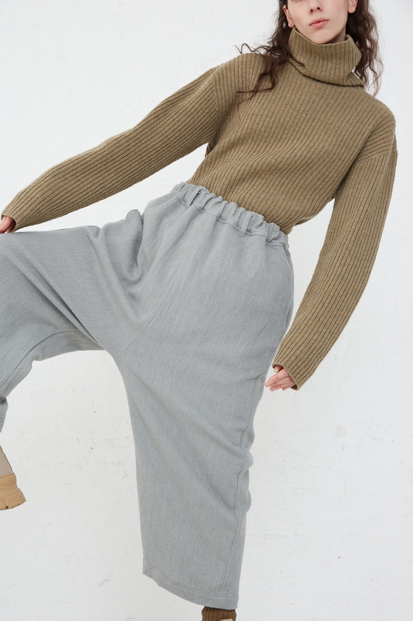 The model is wearing a turtle neck sweater and grey wide leg pants made of Merino Wool Orihimedaki Pant in Blue by Ichi Antiquités.