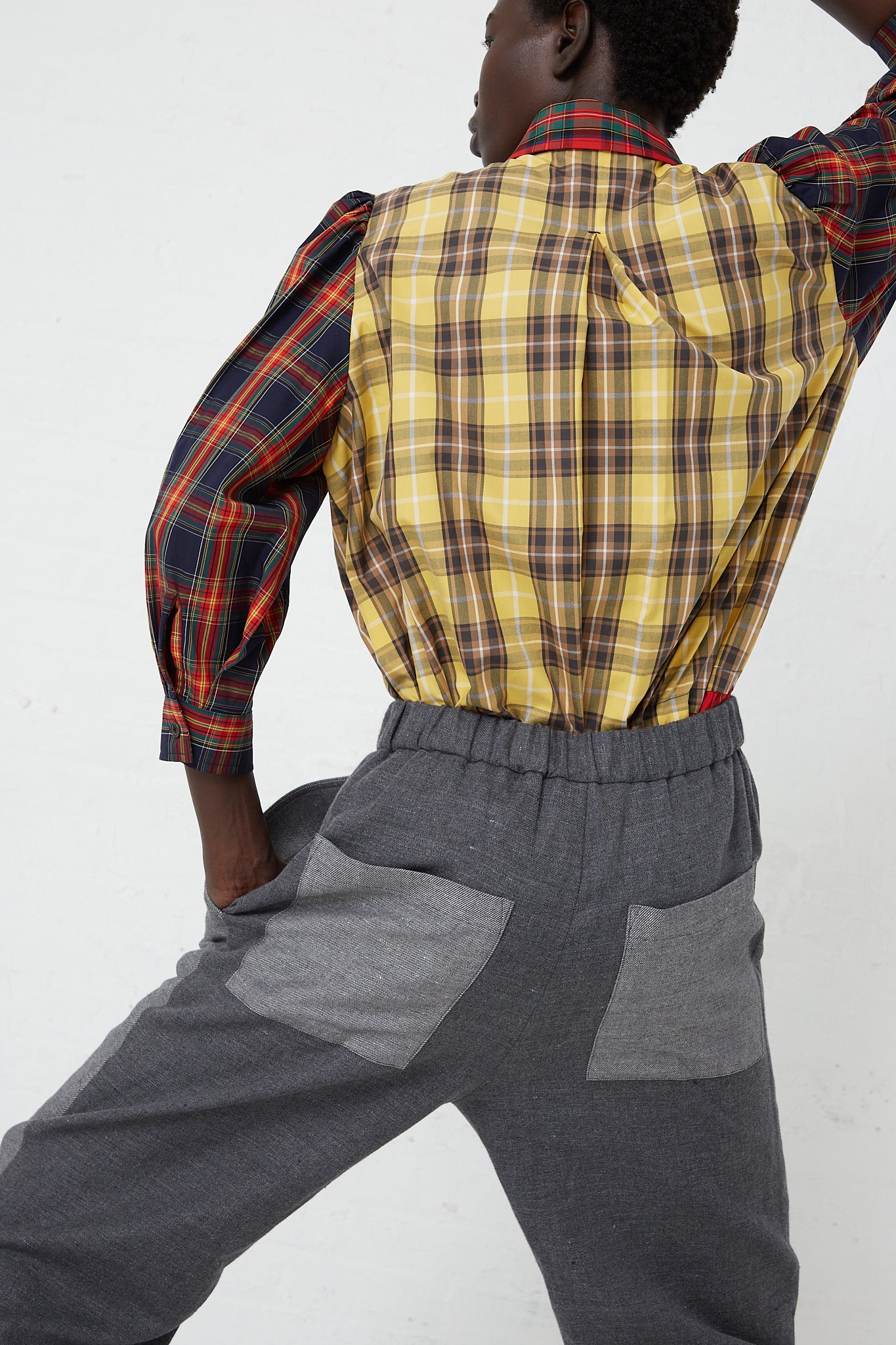 A model in a plaid Japanese KasMaria flannel shirt with adjustable ties and Cotton Linen Flannel Front Patch Pant in Gray sweatpants. Back view.