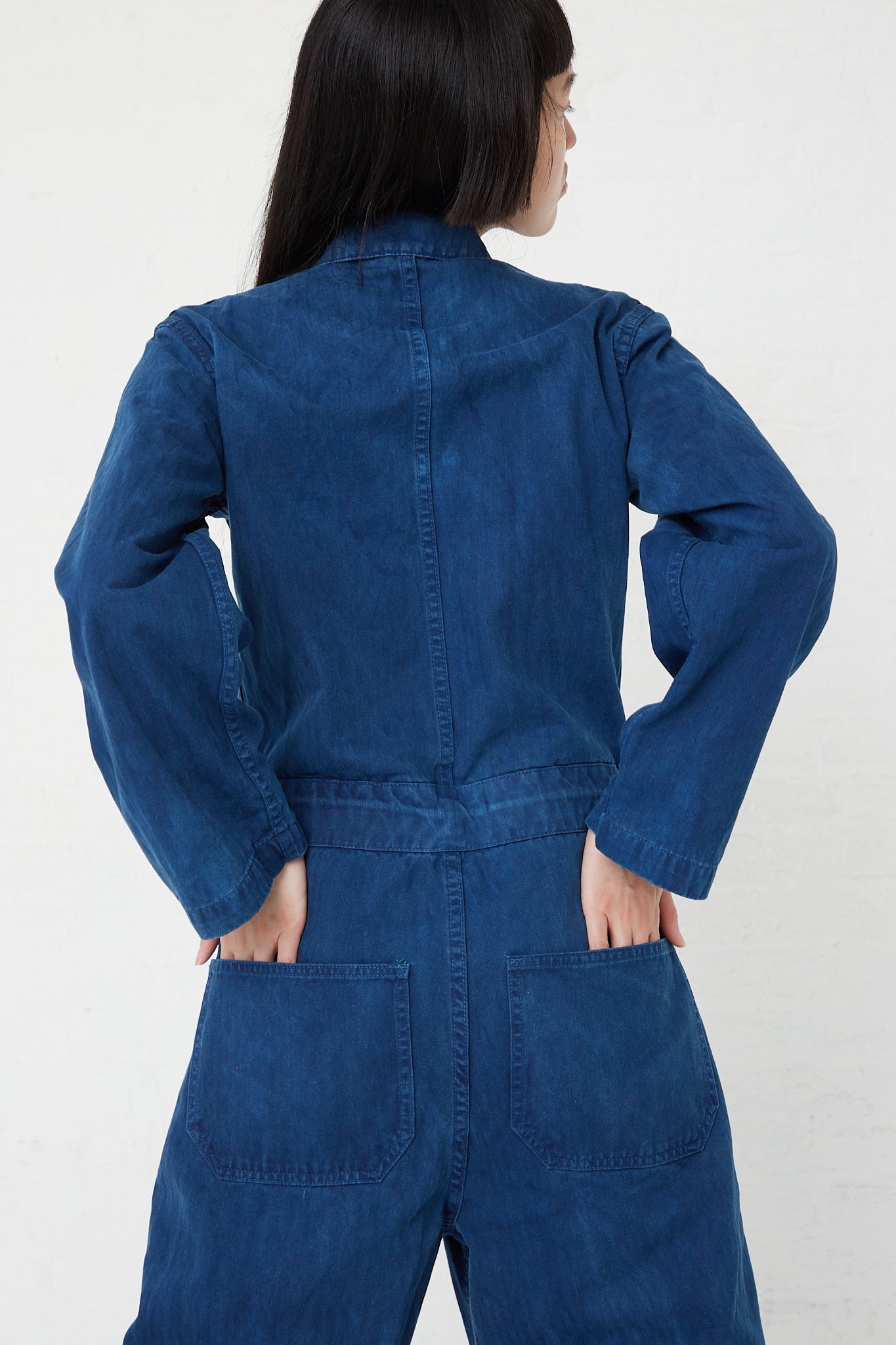 A woman wearing an As Ever front zip jumpsuit in Indigo. Back view. Up close.