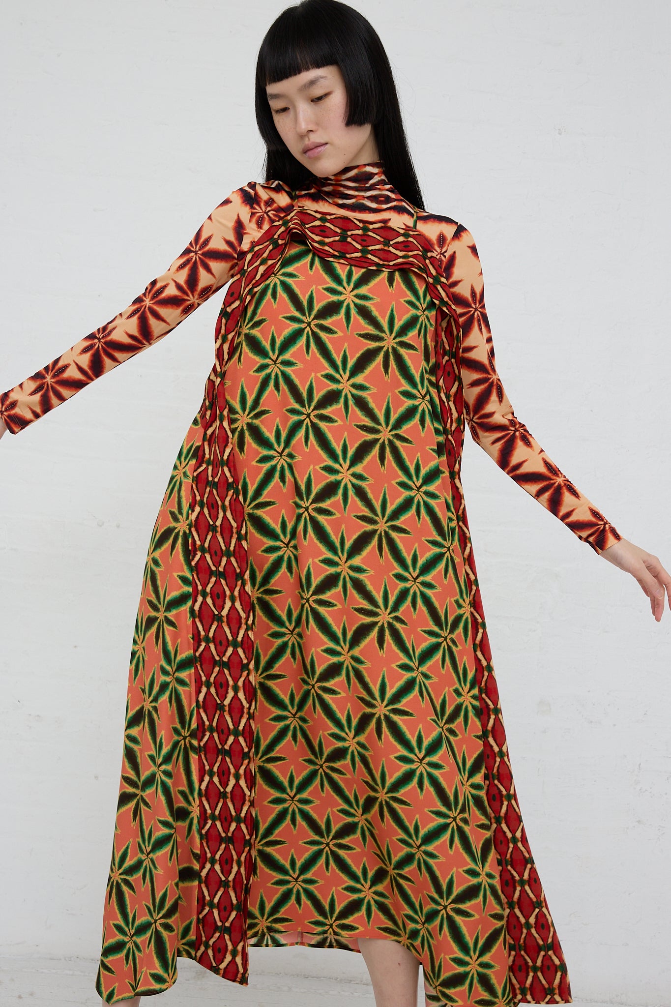 A woman in the Ulla Johnson Lily Dress in Fresco, a square neckline midi dress made of shibori printed satin-back crepe in orange and green.