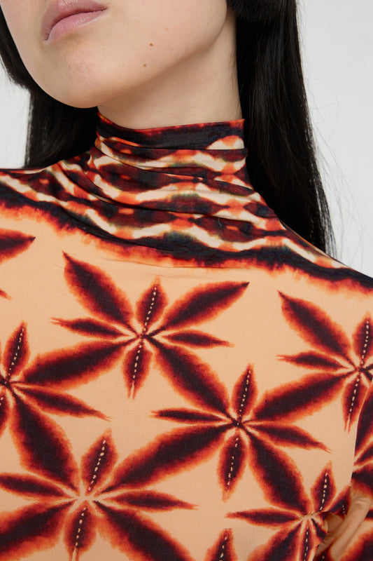 A woman wearing an Ulla Johnson Aurelia Turtleneck in Andromeda made of printed tricot jersey in a black and orange pattern. Front view and up close view of turtleneck.