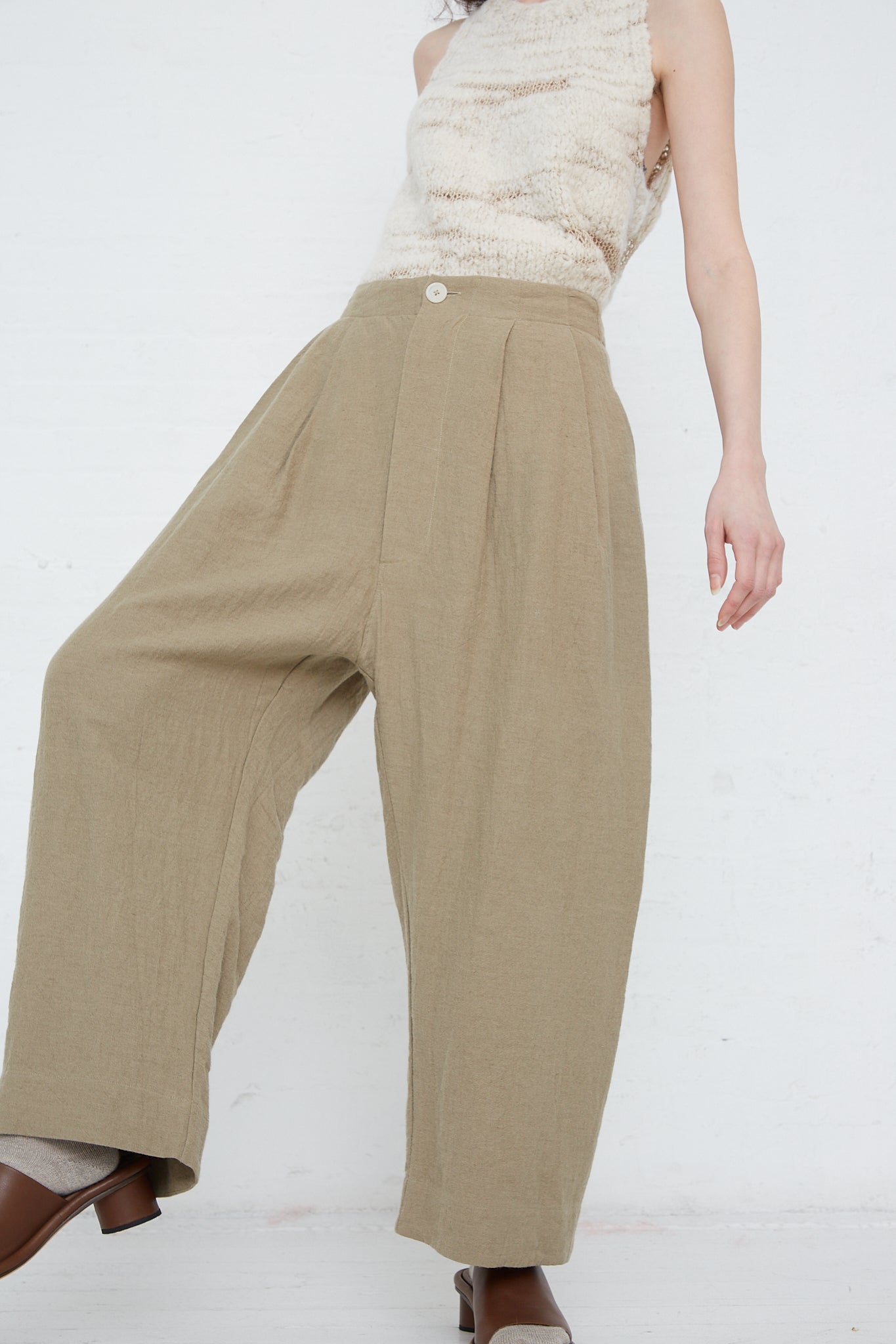 A woman is standing in a white room wearing Lauren Manoogian's Linen and Wool Como Trouser in Clay.