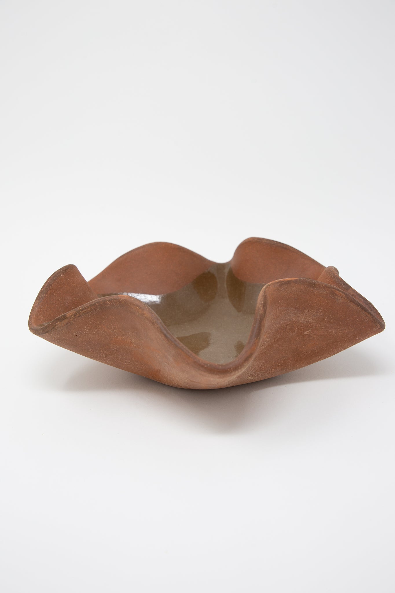 A Ruffle Bowl in Terracotta by Lost Quarry, with a curved shape, hand-built sculpture functional object on a white background.