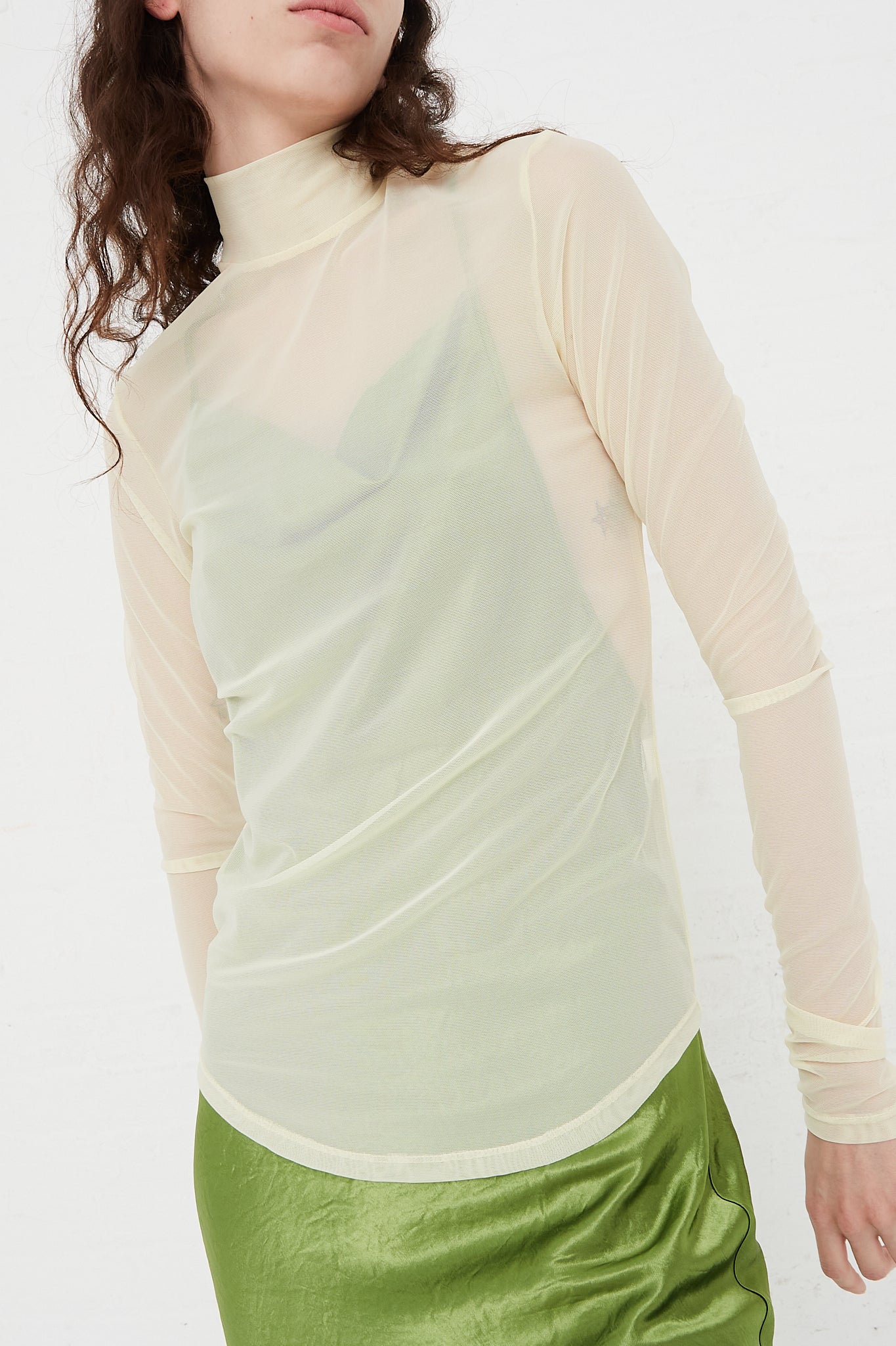 A model wearing a green skirt and a green turtle neck top, designed by the Nomia brand, available at Oroboro store in NYC.