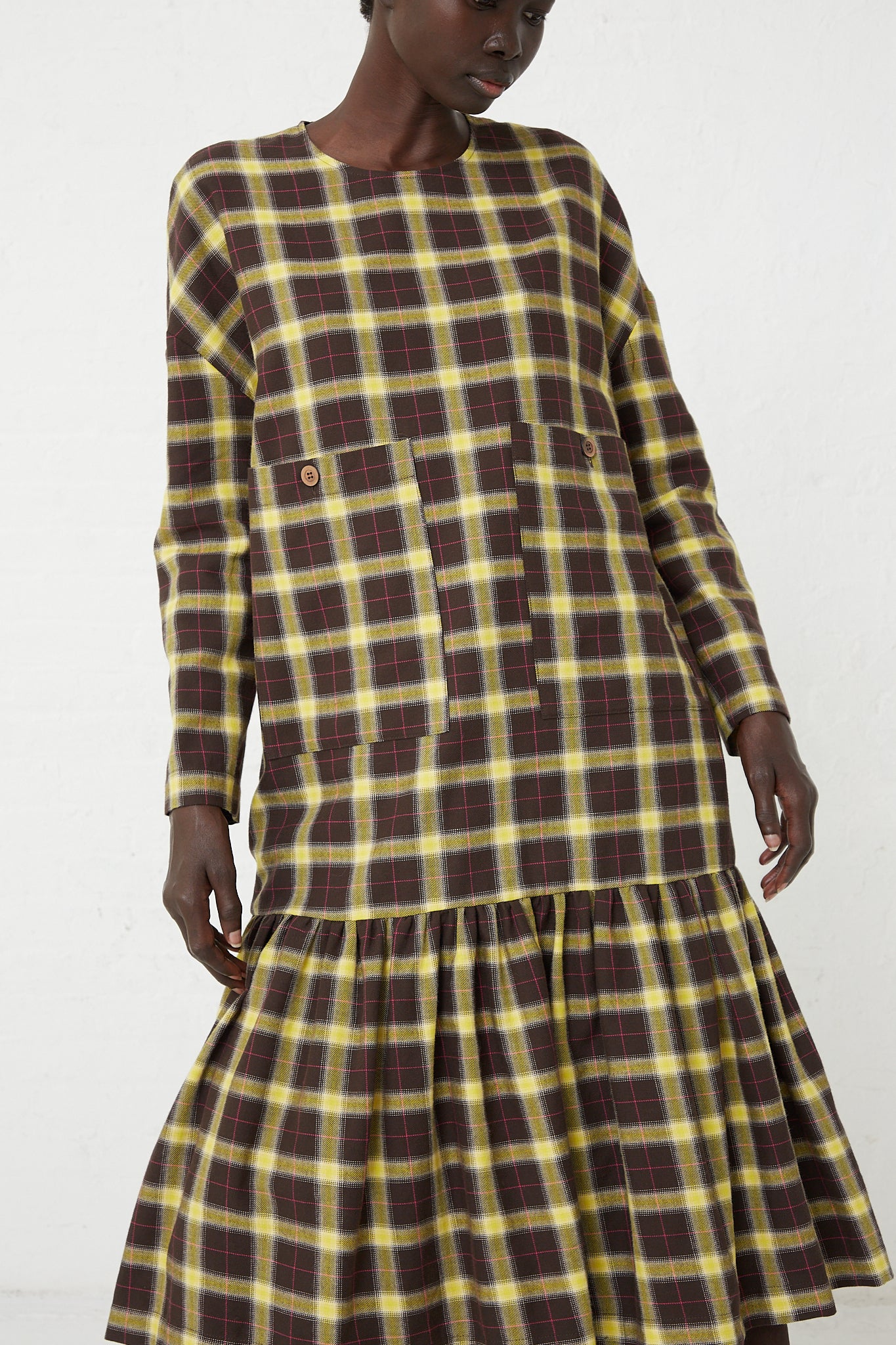 The model is wearing a Fun Dress in Check Brown, Yellow and Pink by AVN, featuring oversized patch pockets.