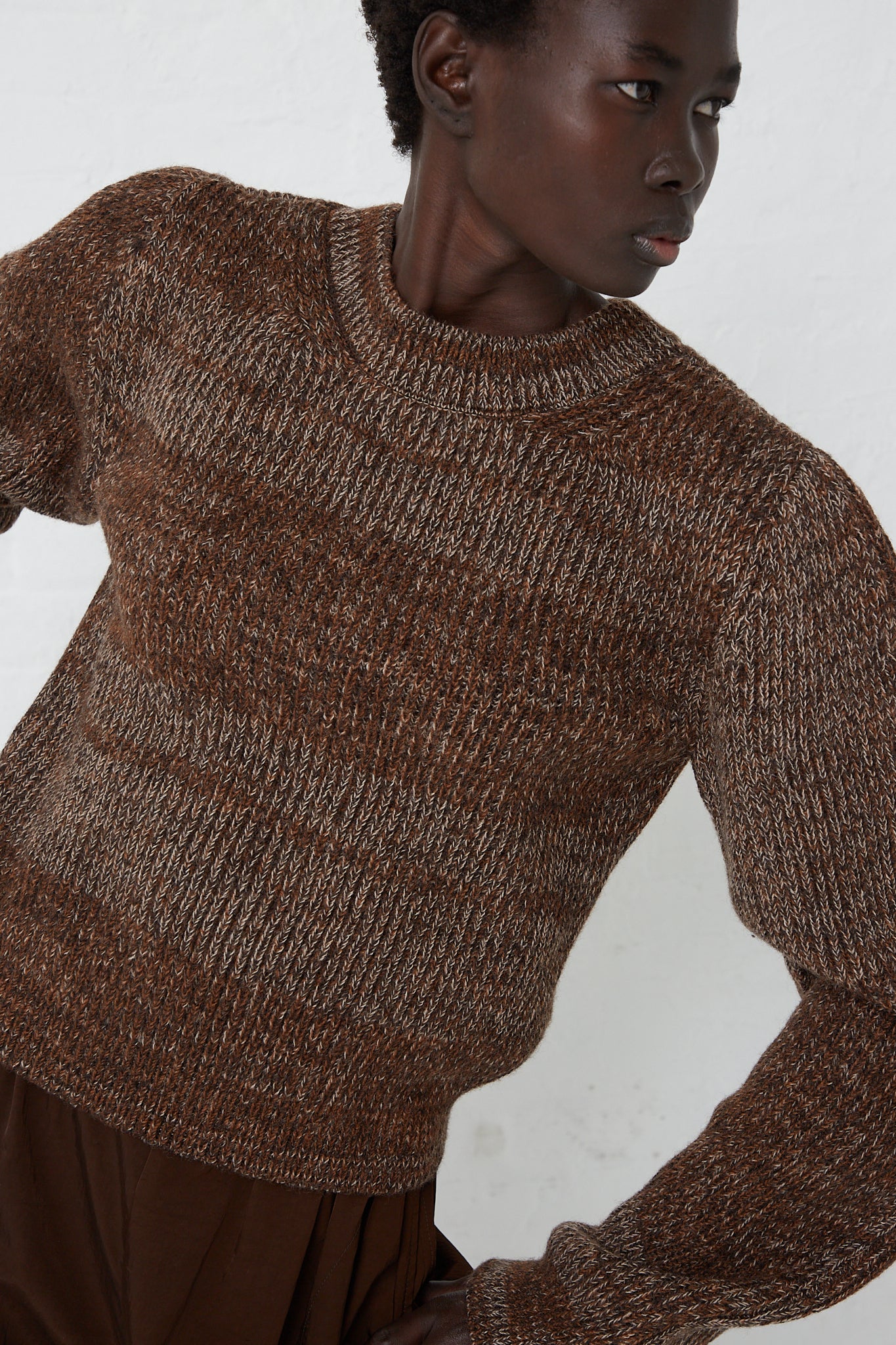 A model wearing a Curved Sleeve Sweater in Oak made by Veronique Leroy, a relaxed fit brown sweater made of virgin wool.