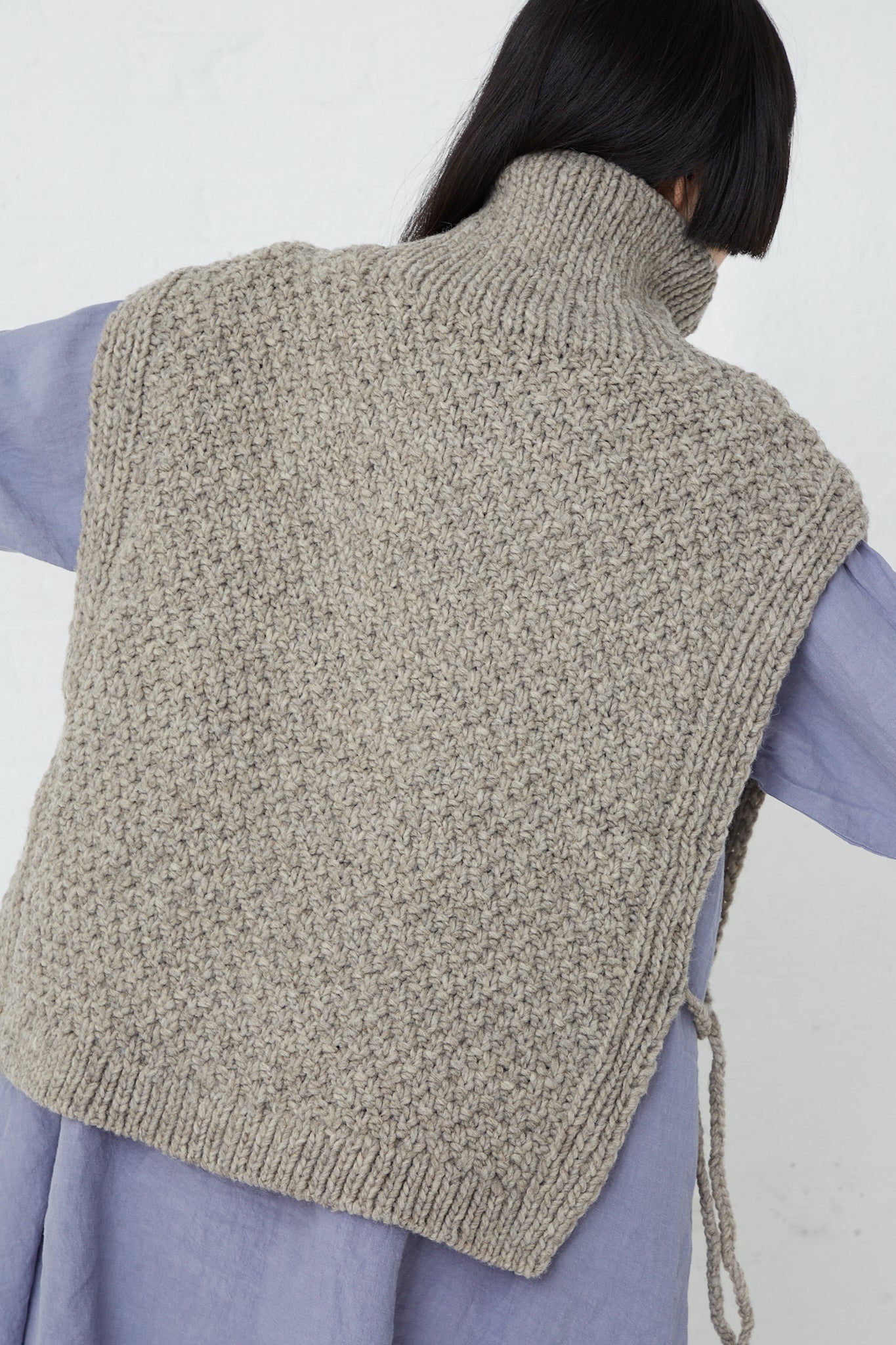 A woman showcasing a Peruvian Wool Hand Knitted Cable Stitch Vest in Beige made from ethically raised sheep wool, featuring a beautifully intricate cable stitch pattern, by nest Robe.
