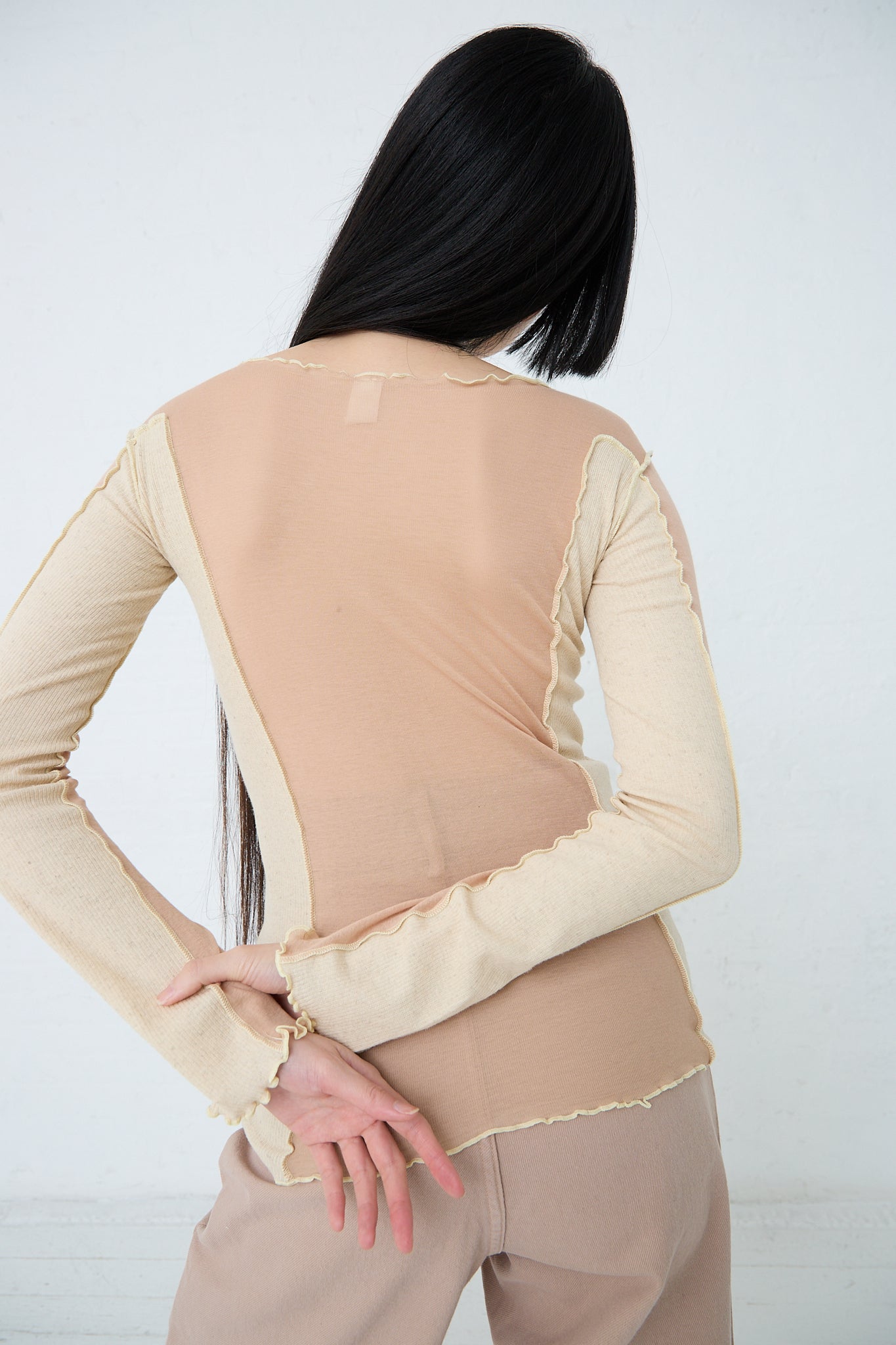 A woman wearing the Baserange Sun Longsleeve in Rosy Camel (Pink) made from organic cotton. Back view.
