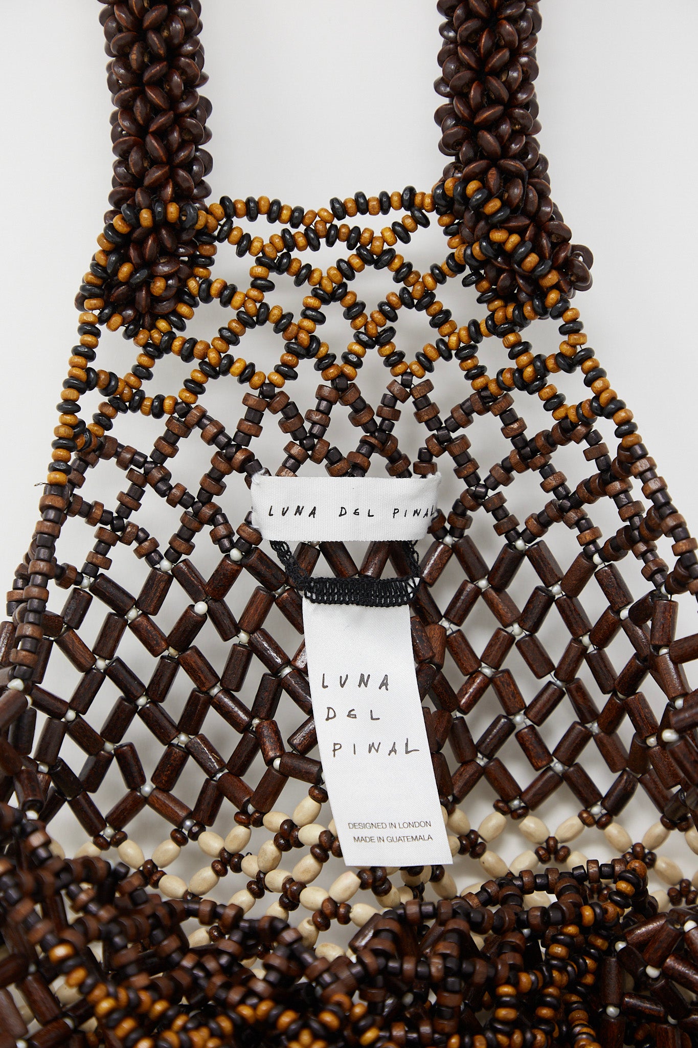 This Luna Del Pinal Medium Wooden Beaded Bag in Bone Brown showcases a beautiful combination of brown and white beads, accented with a small tag.