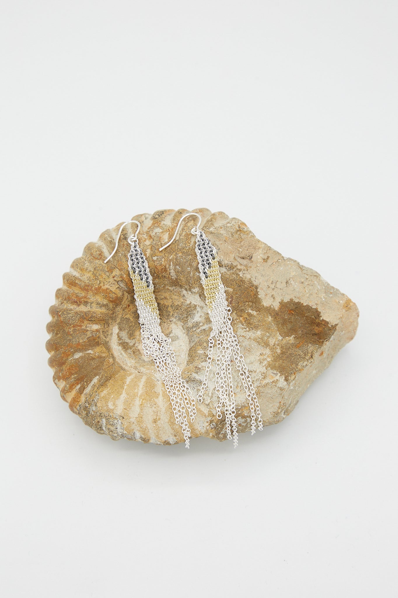 A pair of Stephanie Schneider sterling silver earrings in silver oxidized and gold-plated silk with tassels on a shell.