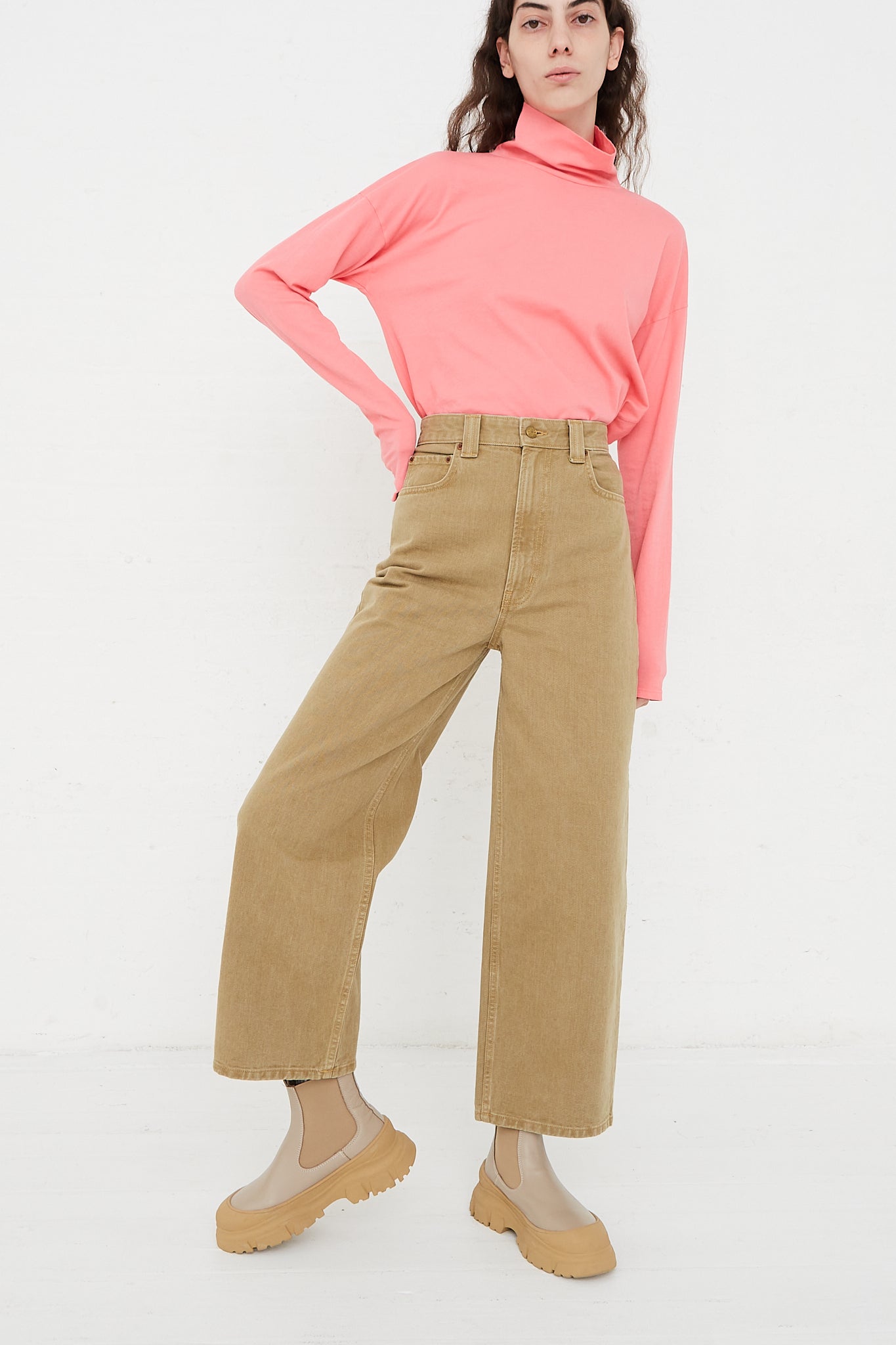 A model wearing a pink turtle neck top and tan corduroy pants for B Sides' Cotton Easy Jean Mid Relaxed in Stone Rinse.