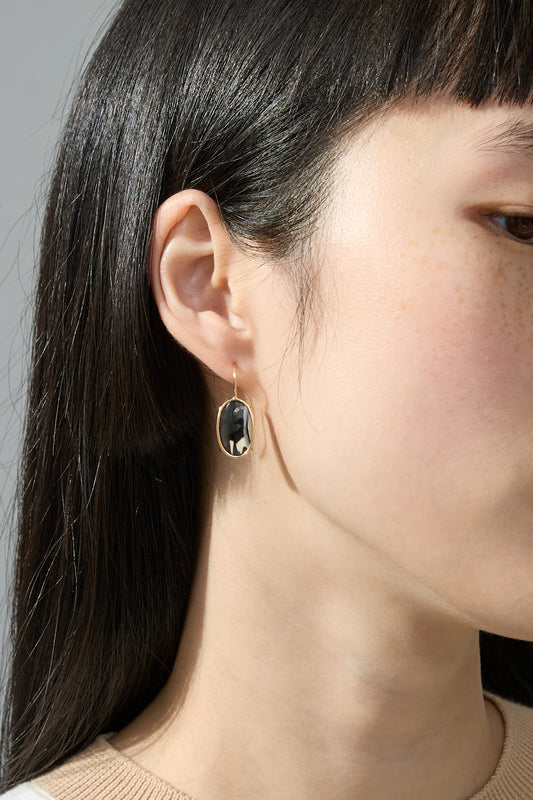 The model is wearing a pair of 14K Floating Drop Earrings in Cowrie Shell by Mary MacGill with a black stone.