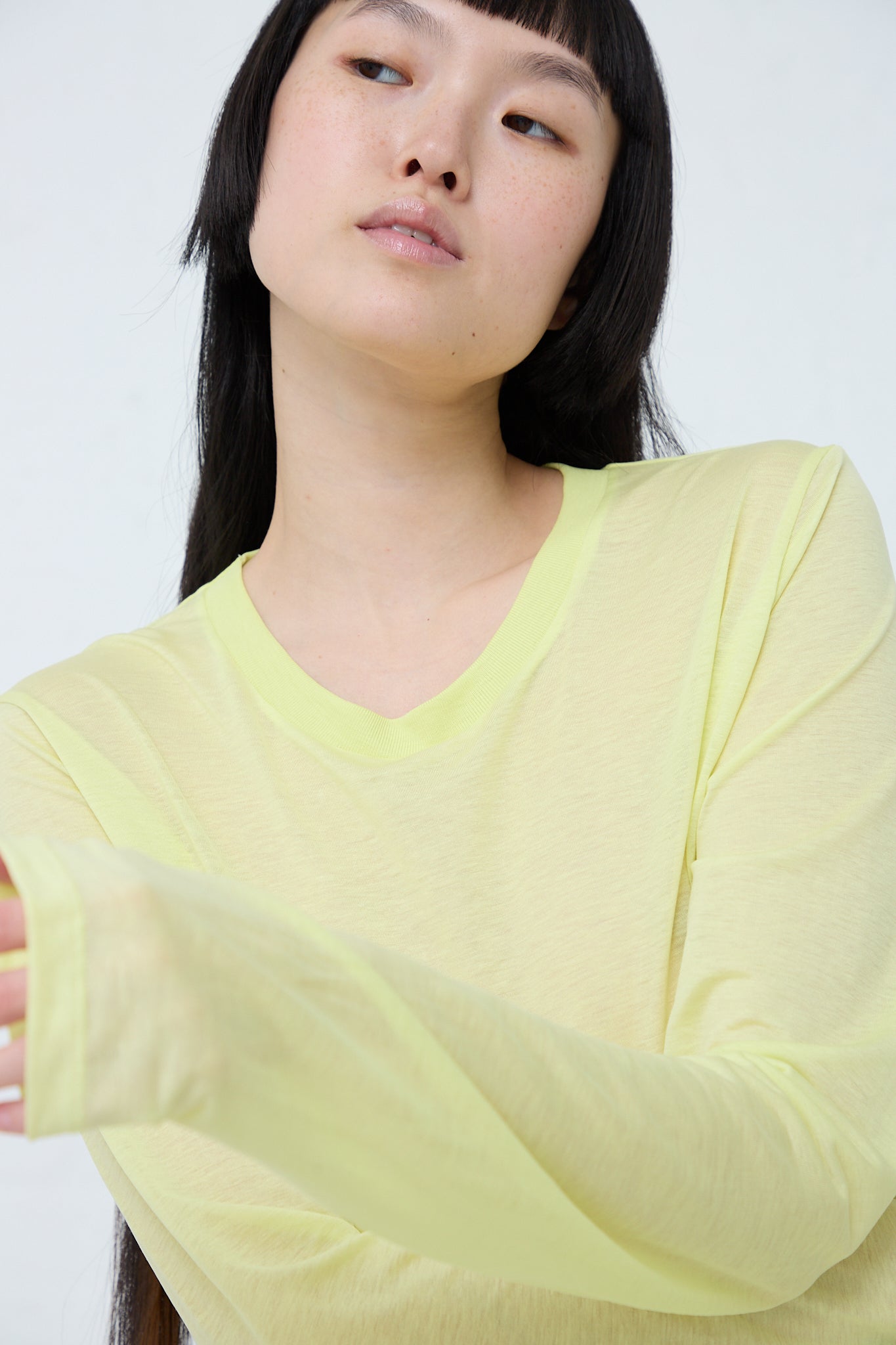 A woman in a sustainable Baserange Bamboo Long Sleeve Tee in Lime is posing for a photo. Up close view.