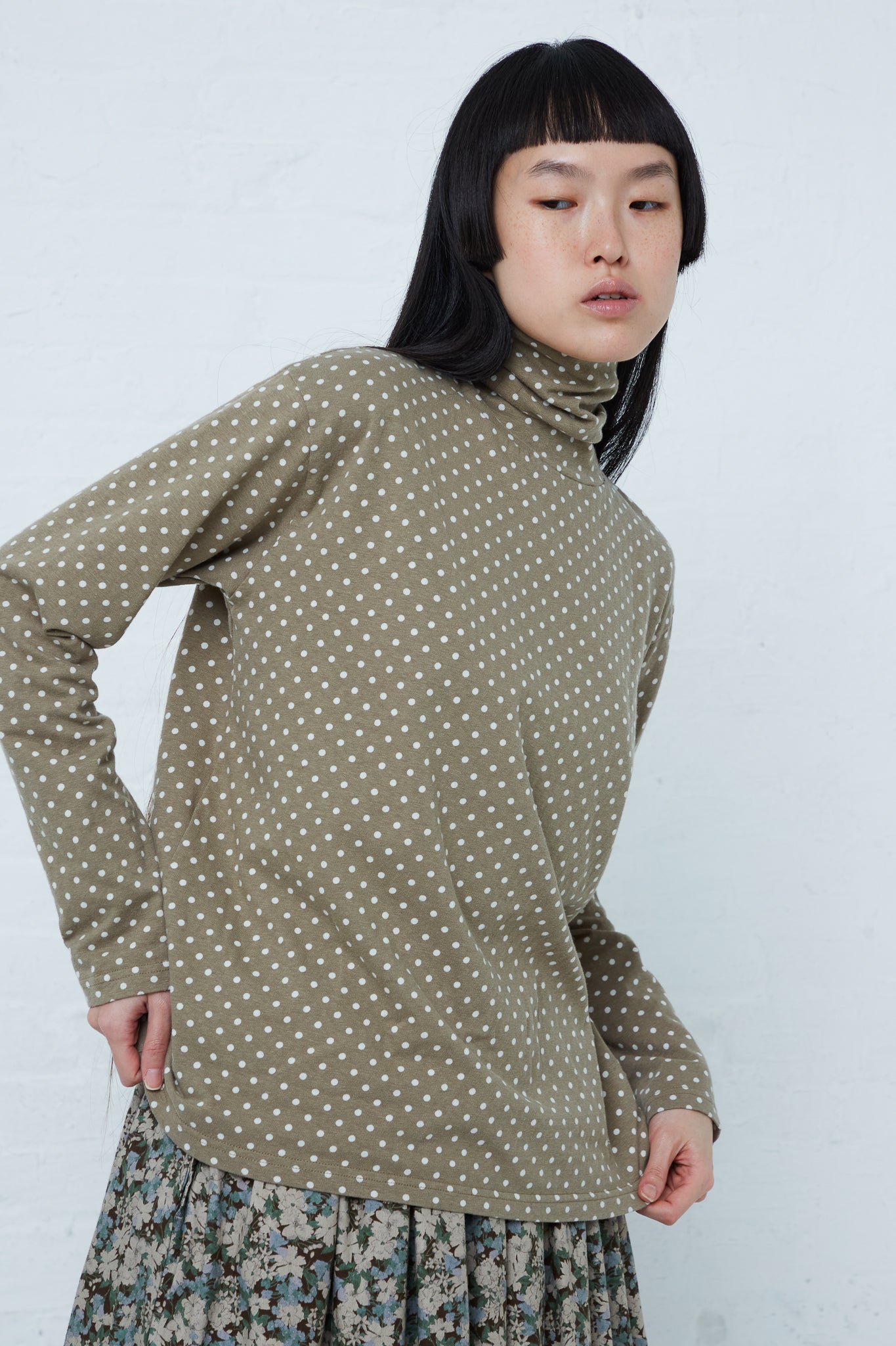 A woman wearing an Ichi Cotton Polka Dot Pullover Turtleneck in Khaki and floral skirt in a relaxed fit.