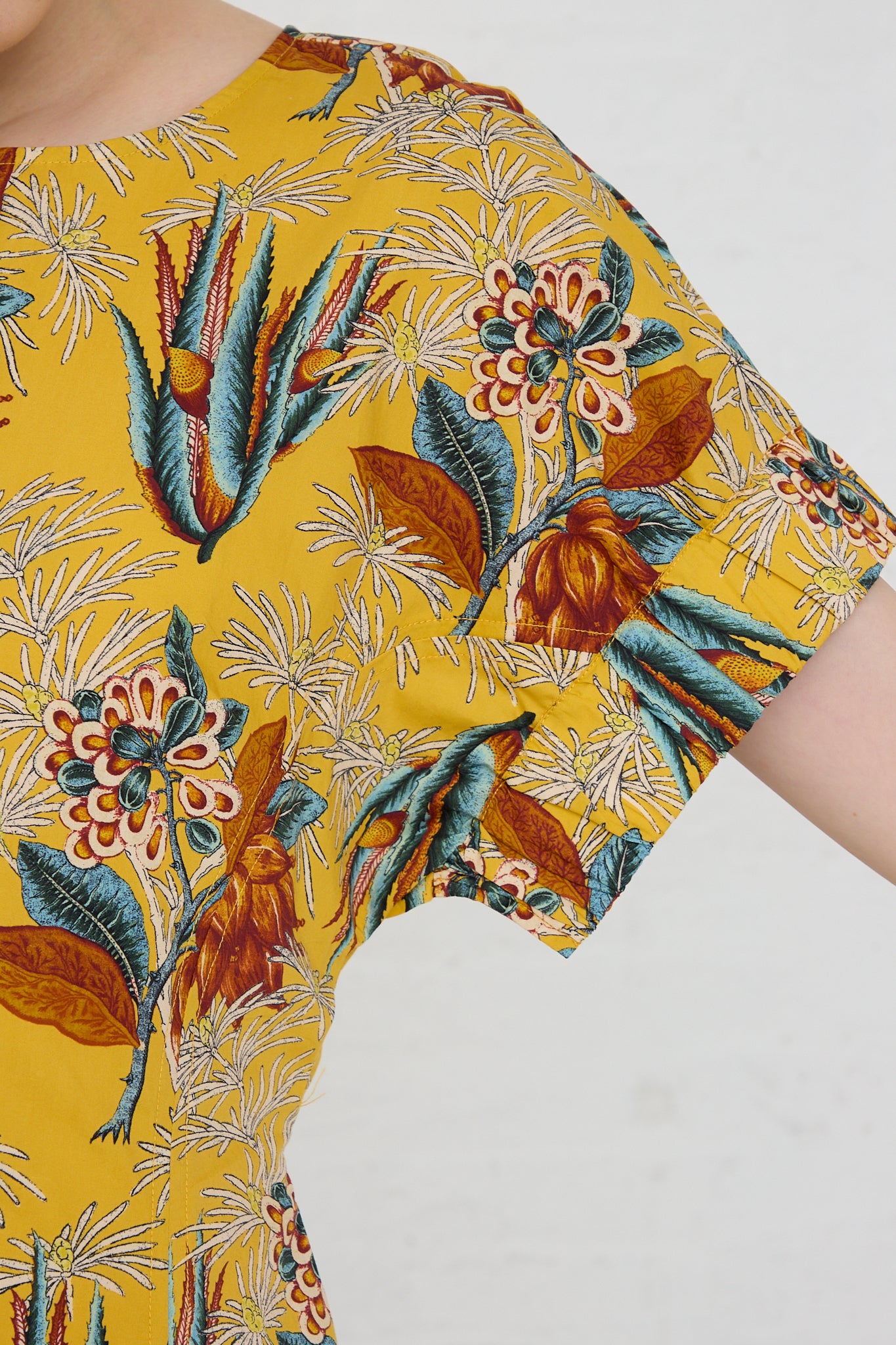 A woman wearing a Devon Dress in Marigold by Ulla Johnson with a tropical print. Up close view of sleeve.