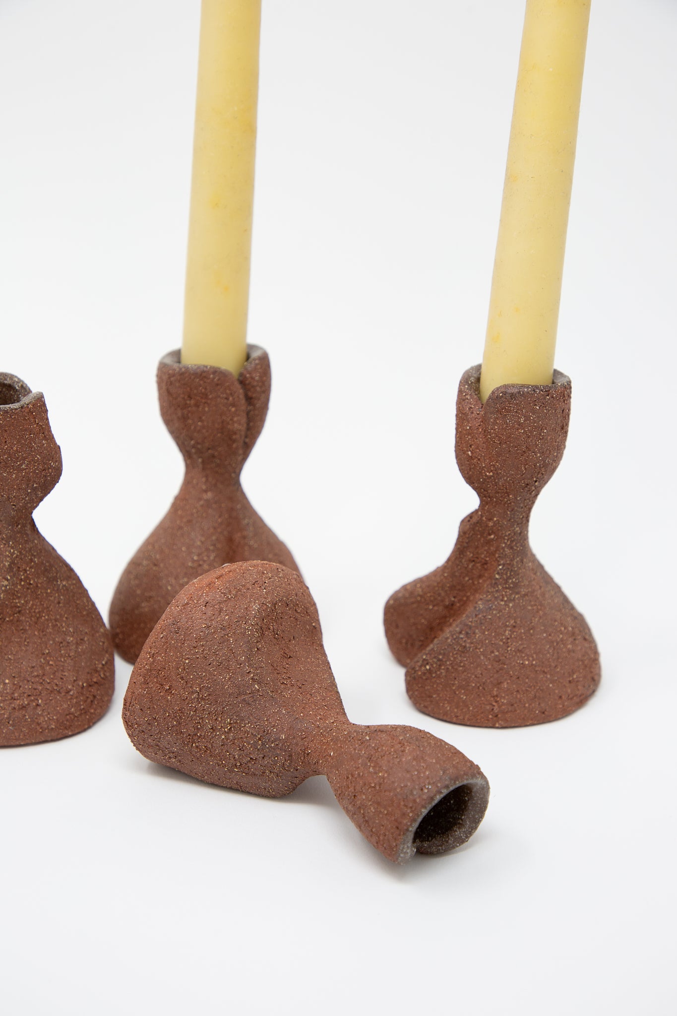 A small group of Lost Quarry terracotta clay candlesticks with a yellow candle.