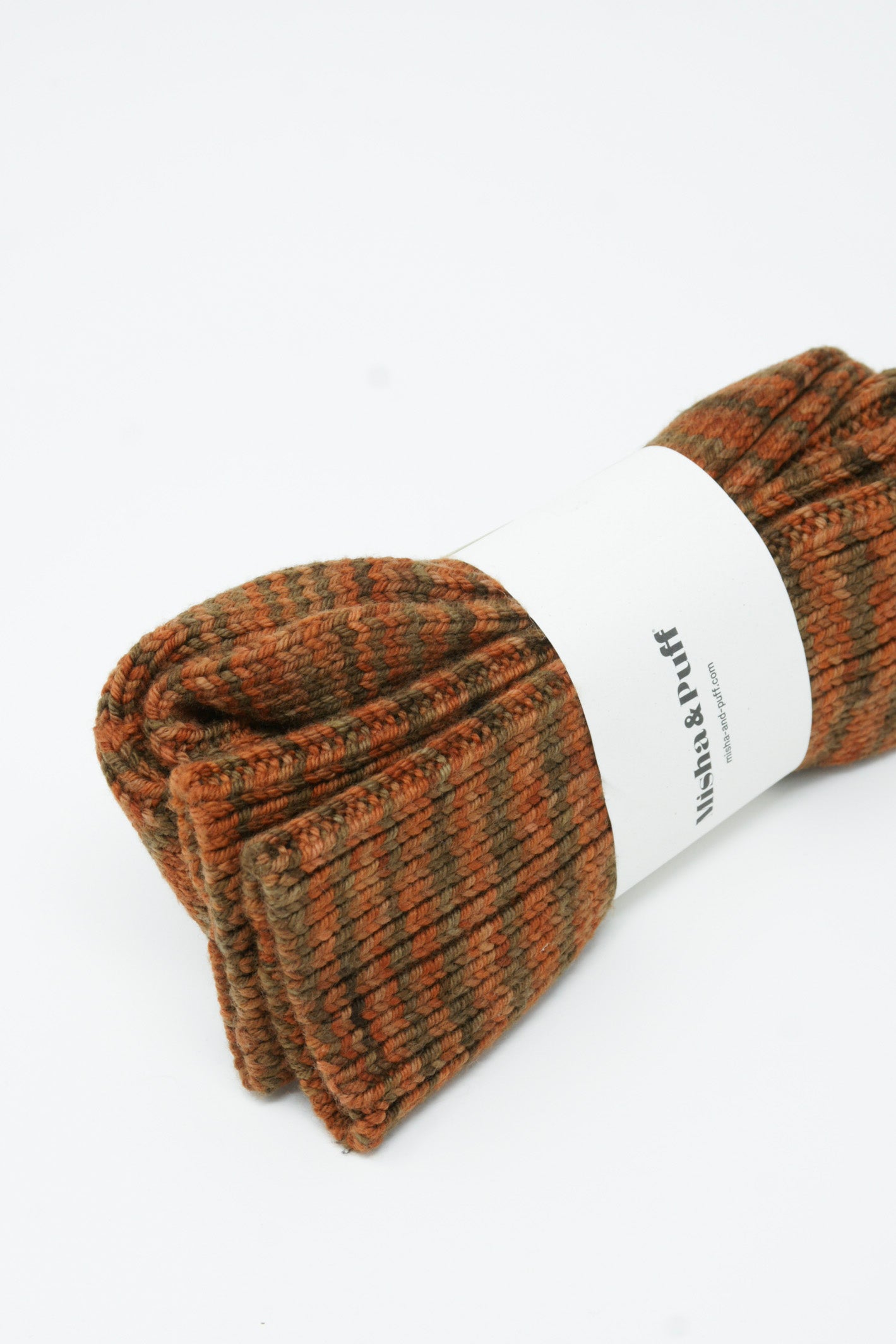 A pair of Misha & Puff Long Wool Socks in Gingerbread Space Dye, featuring a beautiful combination of brown and orange, lying on a crisp white surface.