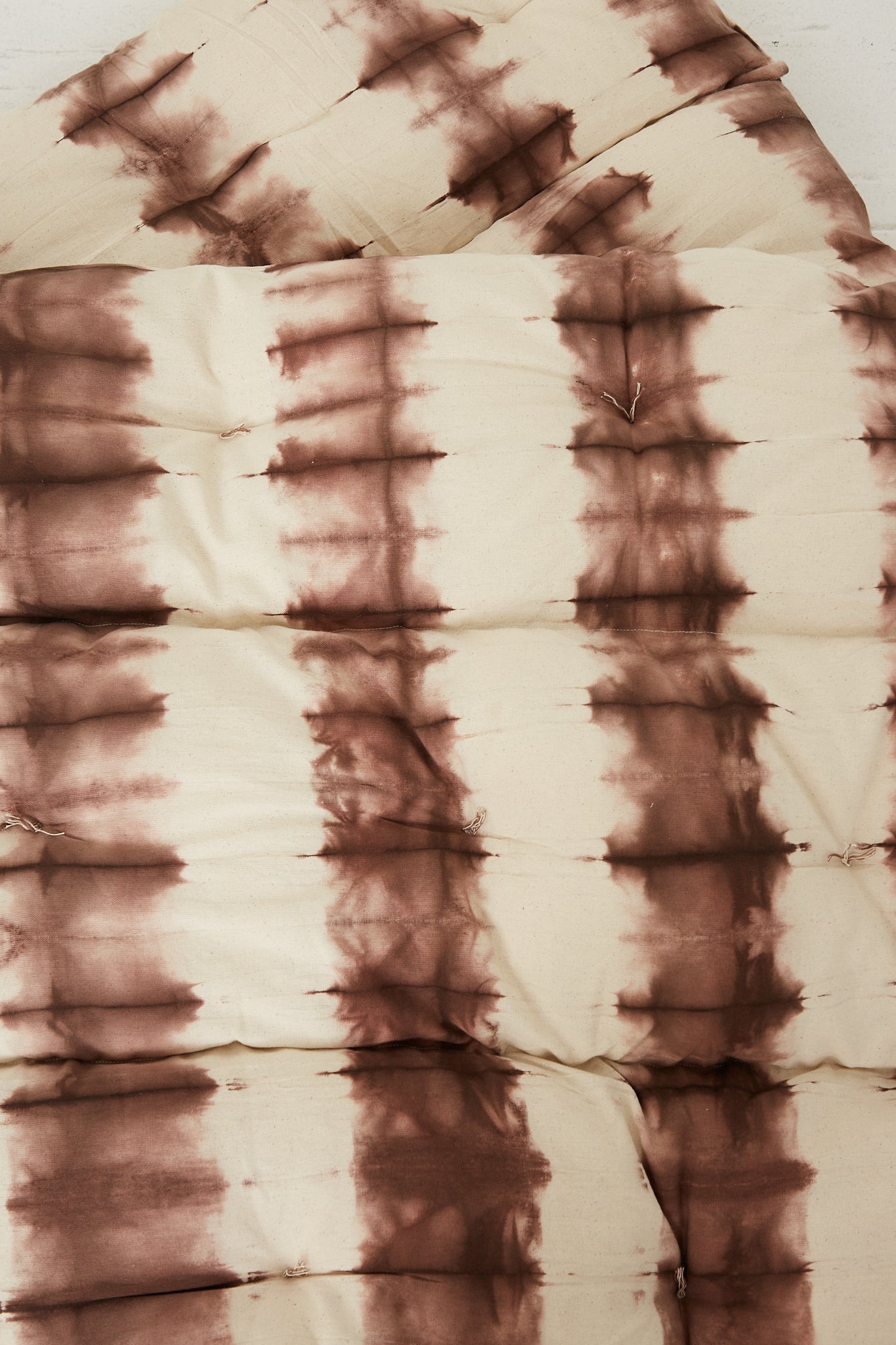 A Tufted Overlay Mattress in Chocolate Tie Dye adorned with a brown and white hand-dyed cotton Tensira comforter.