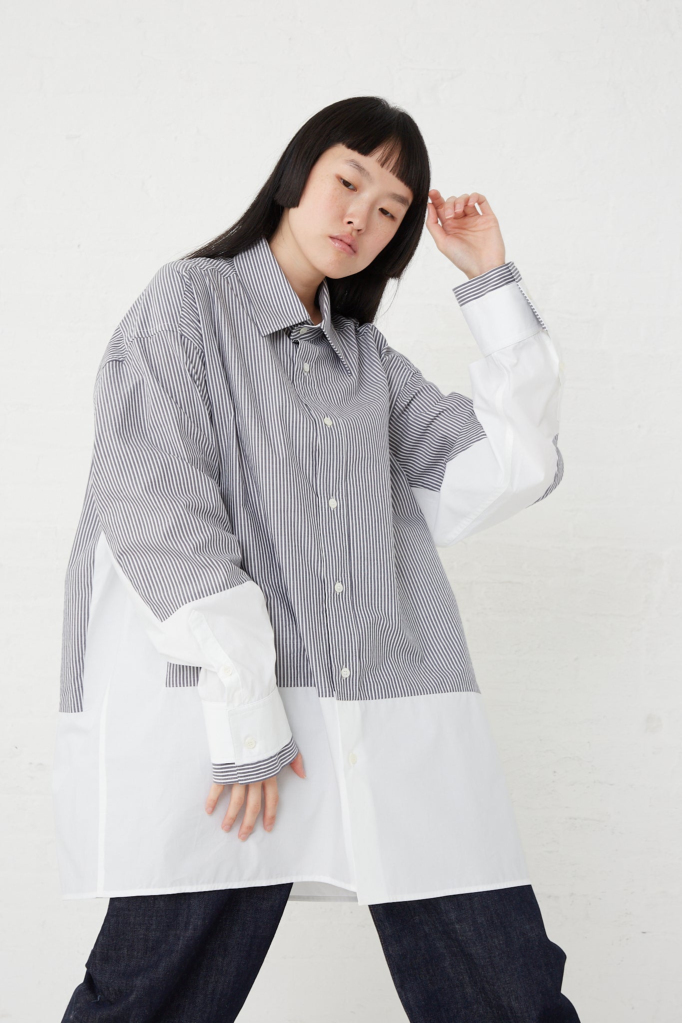 The model is wearing an oversized striped MM6 cotton long sleeved shirt in dark grey and white.
