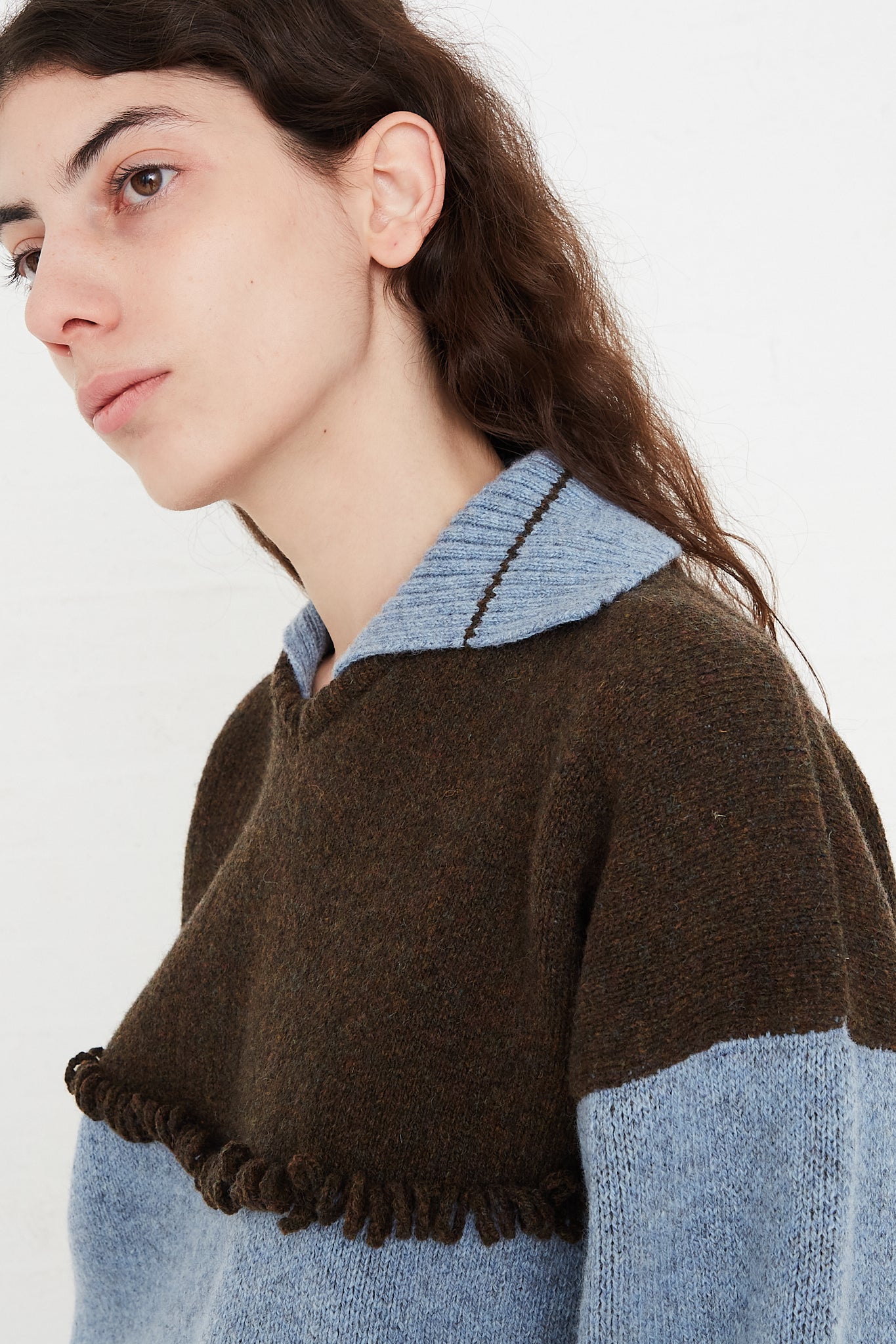 A model wearing a knit pullover sweater in a British wool. Features a polo collar with dropped shoulders and contrast color on top, cuffs and hem. Side view and up close. Showcasing sweater details. Designed by Cawley - Oroboro Store
