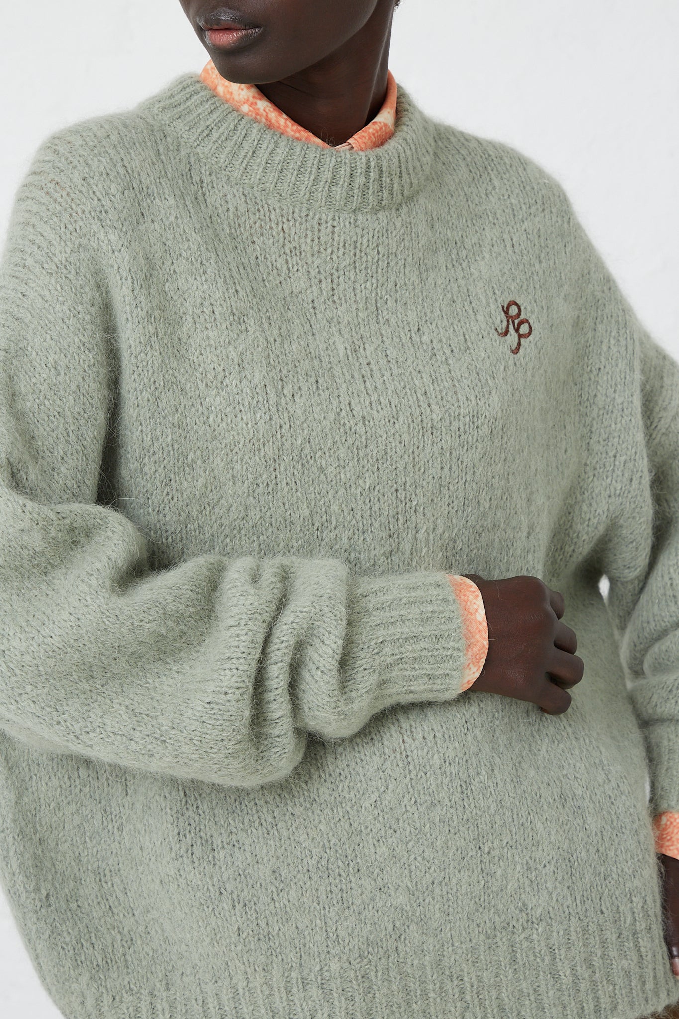 A woman wearing a crew neck Alpaca Blend Toni Sweater in Mint by Rejina Pyo, with an embroidered logo detail.