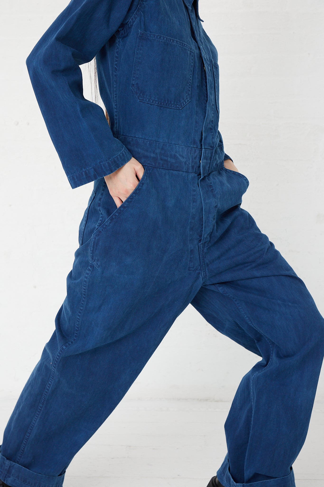 A woman is posing in an As Ever Zip Jumpsuit in Indigo, a hand-dyed Japanese twill jumpsuit.