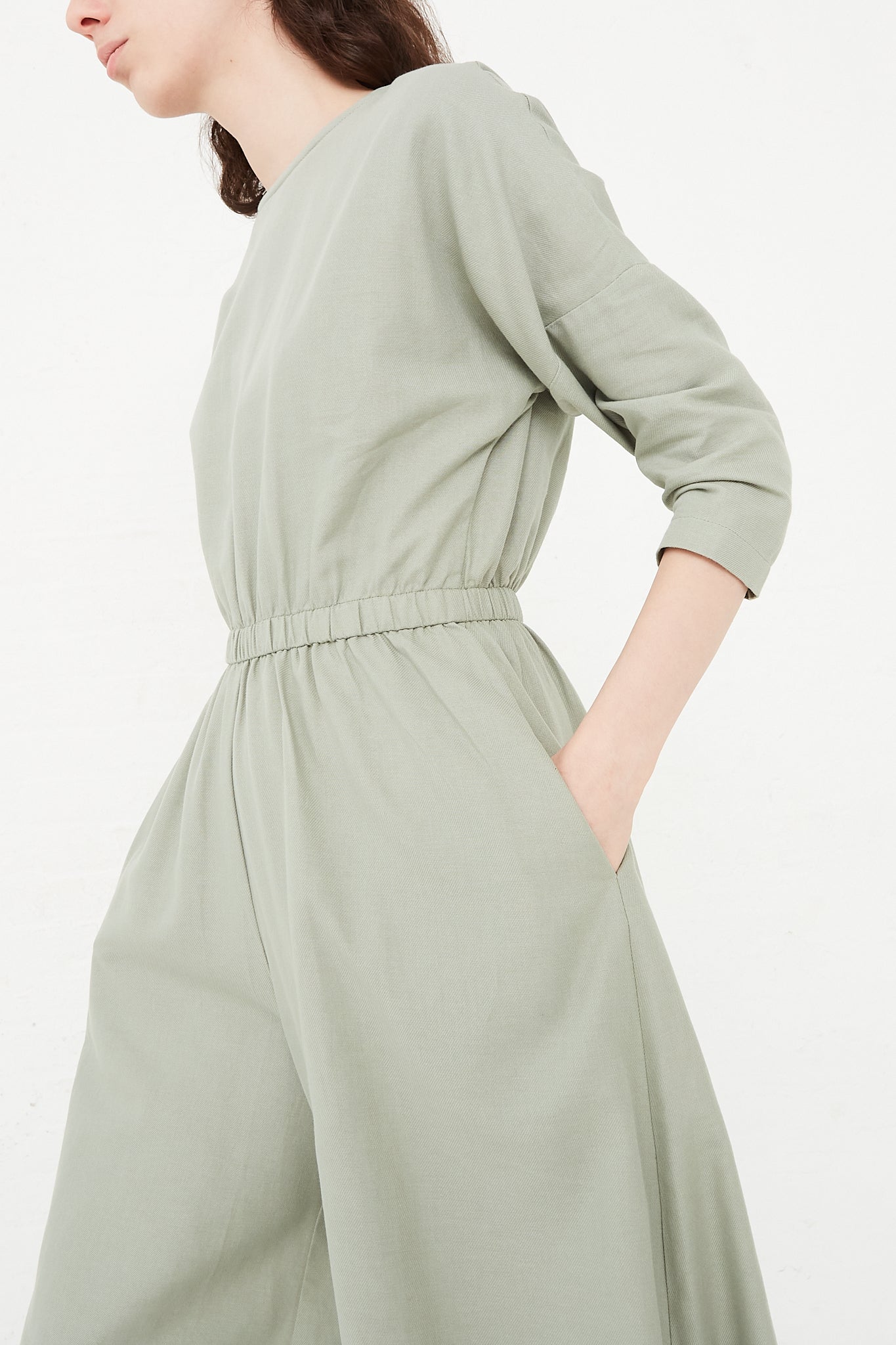 The model is wearing a sage green Black Crane Cotton Twill Wide Culotte Jumpsuit in Agave. Side profile. 