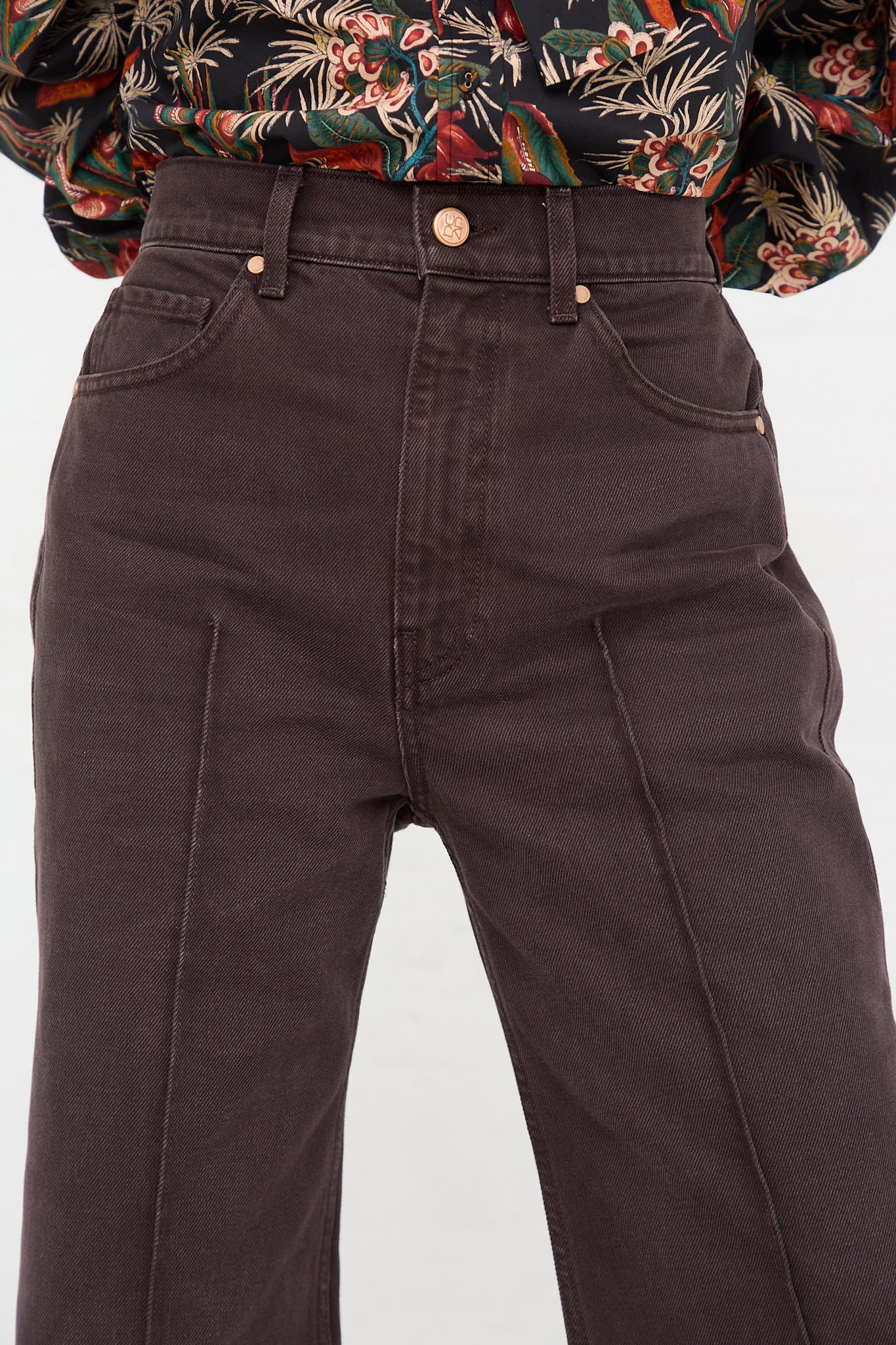 A woman wearing a floral shirt and brown pants, paired with The Genevieve Jean in Mahogany Wash by Ulla Johnson.